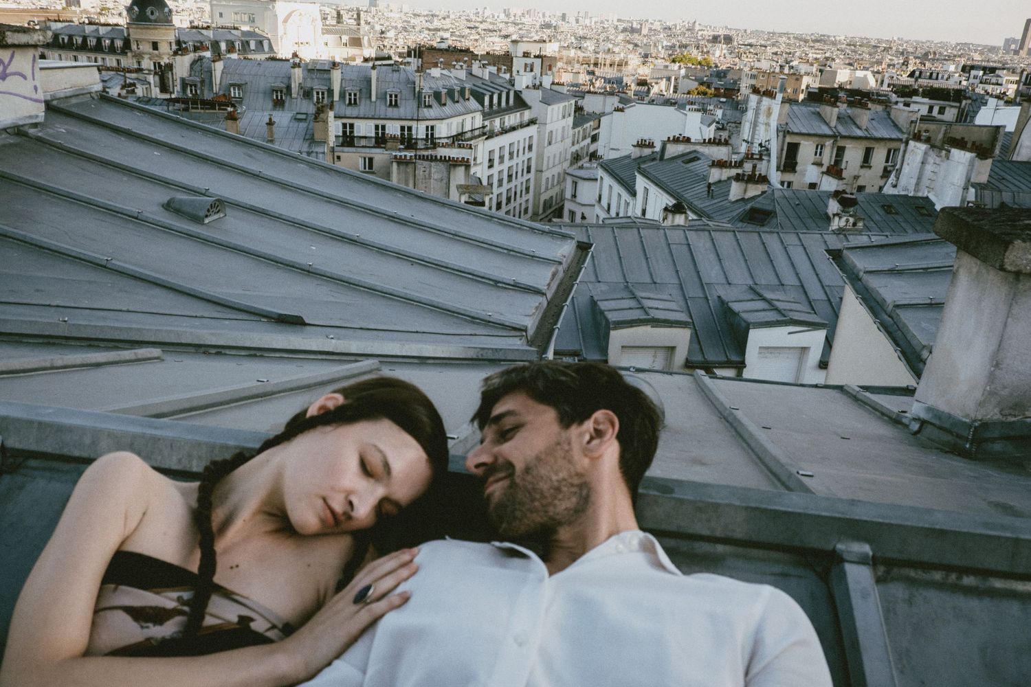 Romantic couple embraces on a rooftop overlooking the historic Parisian cityscape and architecture.