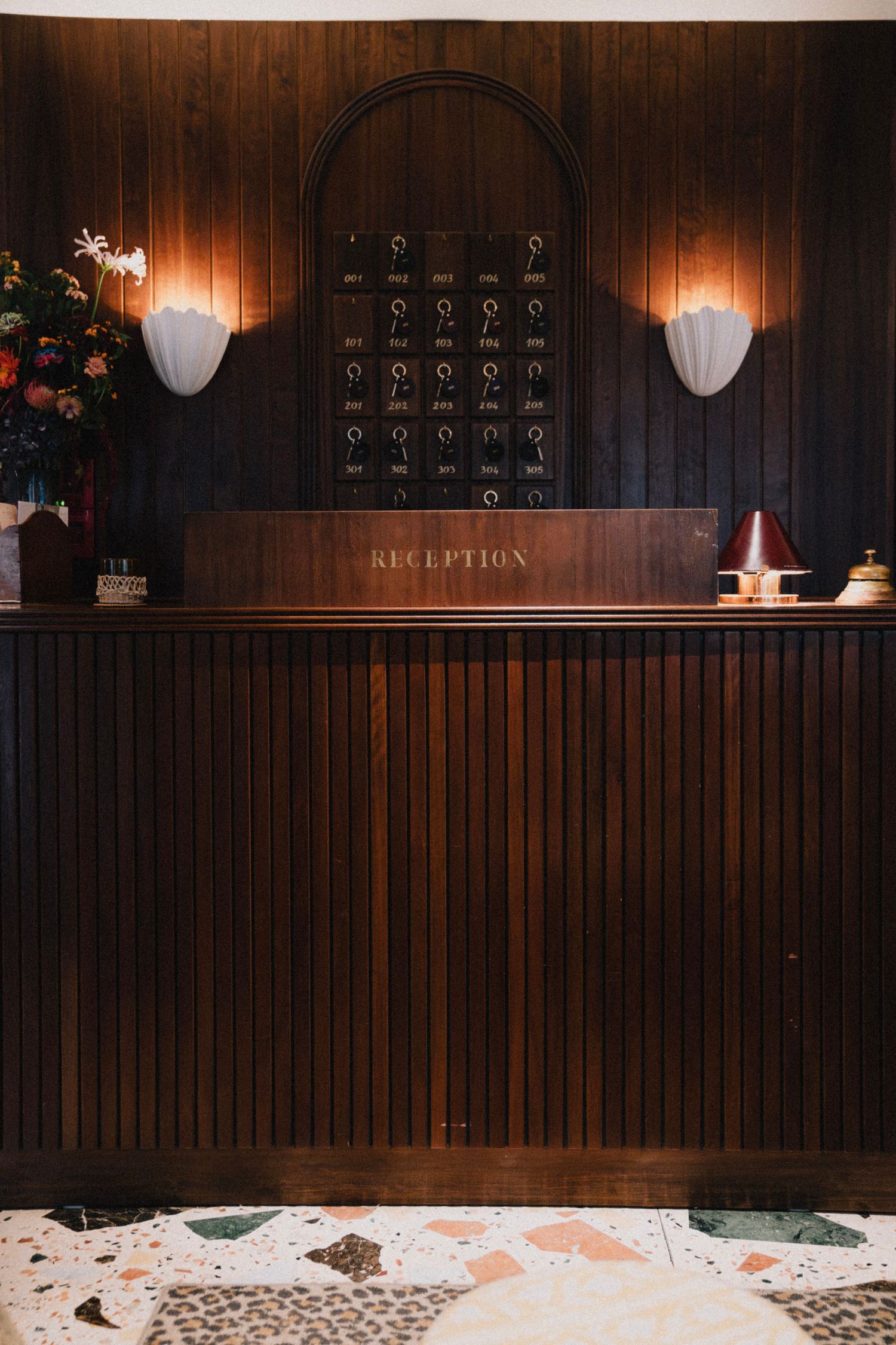 Dark wood paneled reception desk with key hooks and warm lighting in a rustic hotel lobby setting.