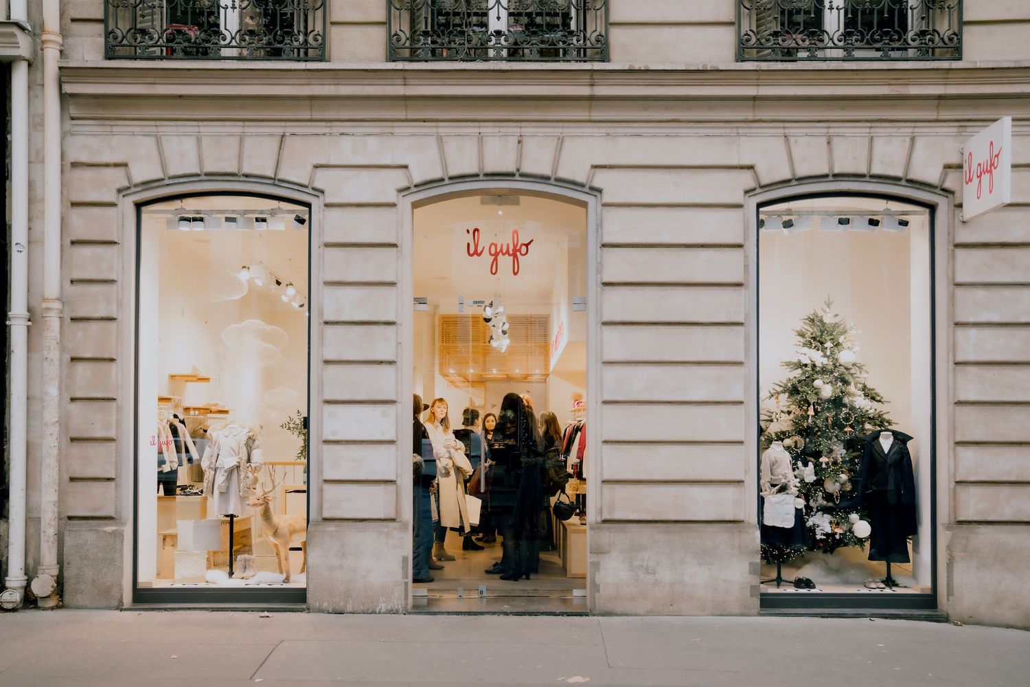 Paris boutique event photo at Il Gufo, with guests seen through windows, unposed and cinematic storytelling perspective