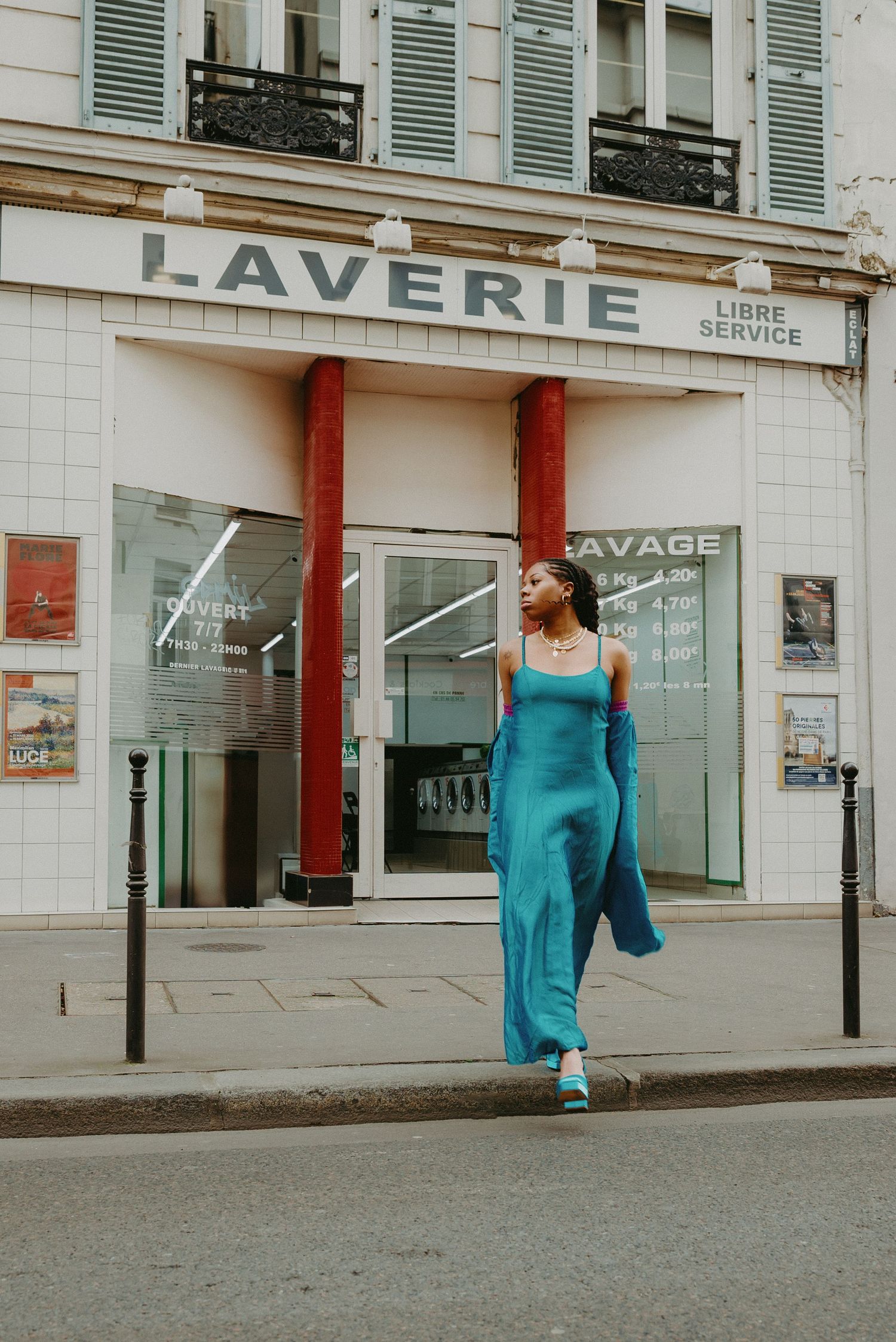 Fashion editorial in Paris with teal jumpsuit, cinematic street style shot in front of a vintage laverie façade.