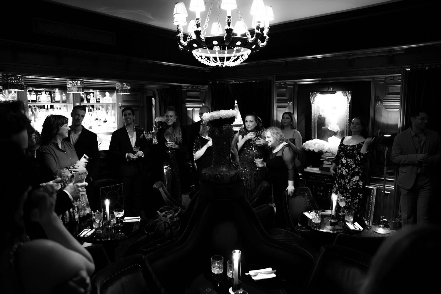 Crystal chandelier illuminates a dark reception venue with guests gathered below.