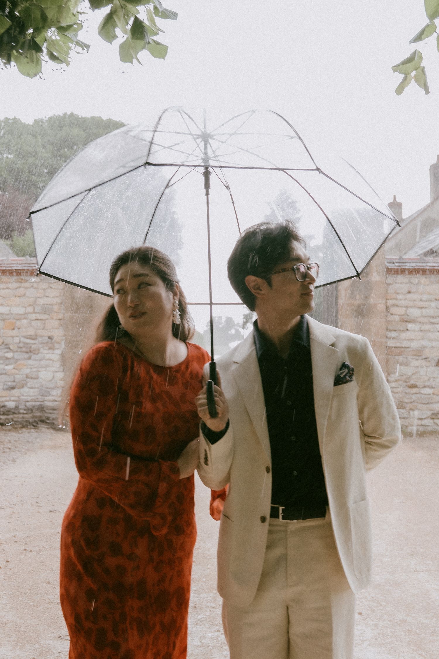 A couple shares playful moments under clear umbrellas on a rainy day.
