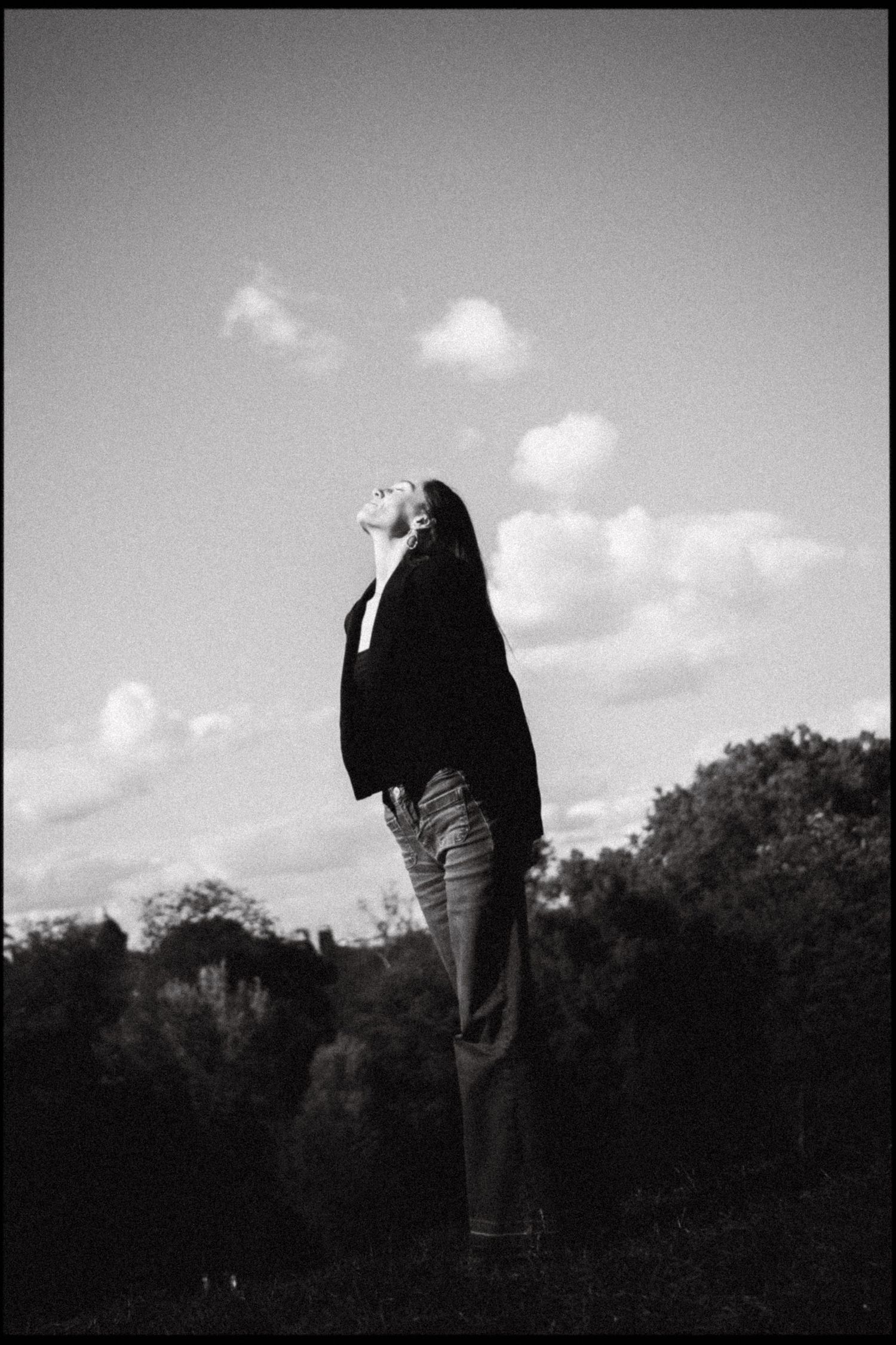 A silhouetted figure stands against a cloudy sky in black and white photography.