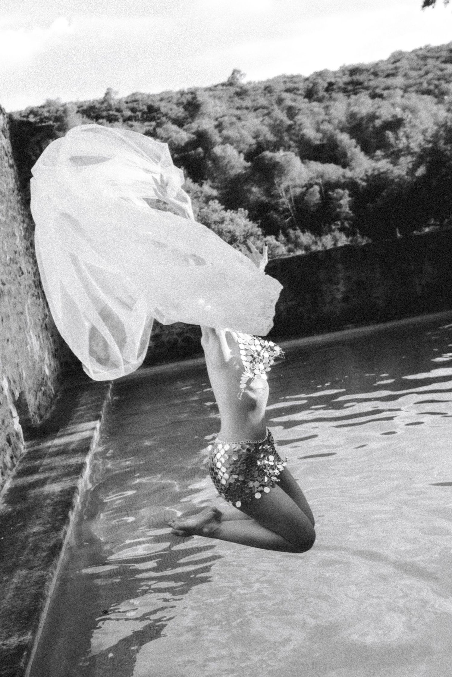 Flowing white dress catches wind in artistic water photoshoot.