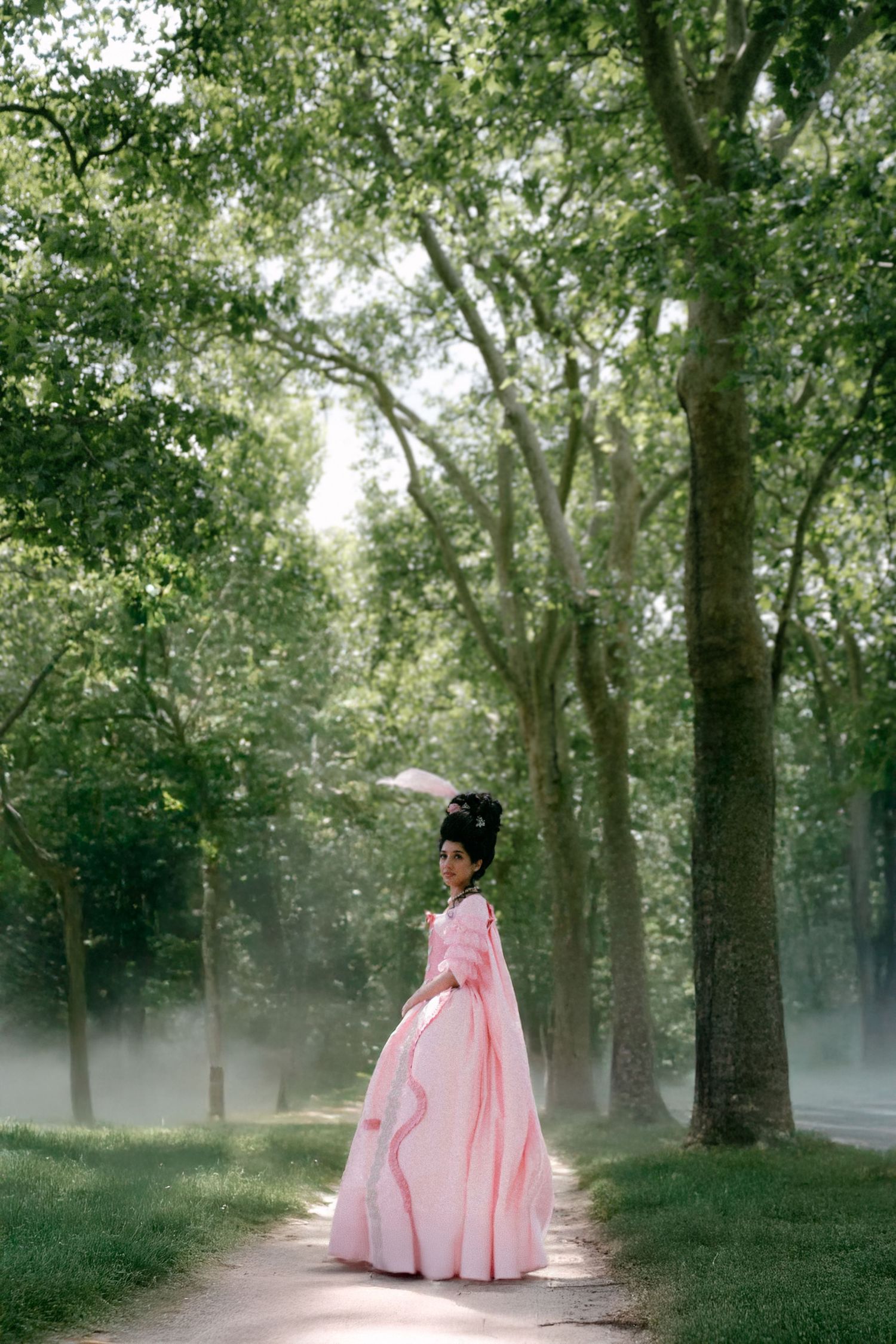 A dreamy scene in a misty forest path with soft sunlight filtering through trees and a pink flowing dress.