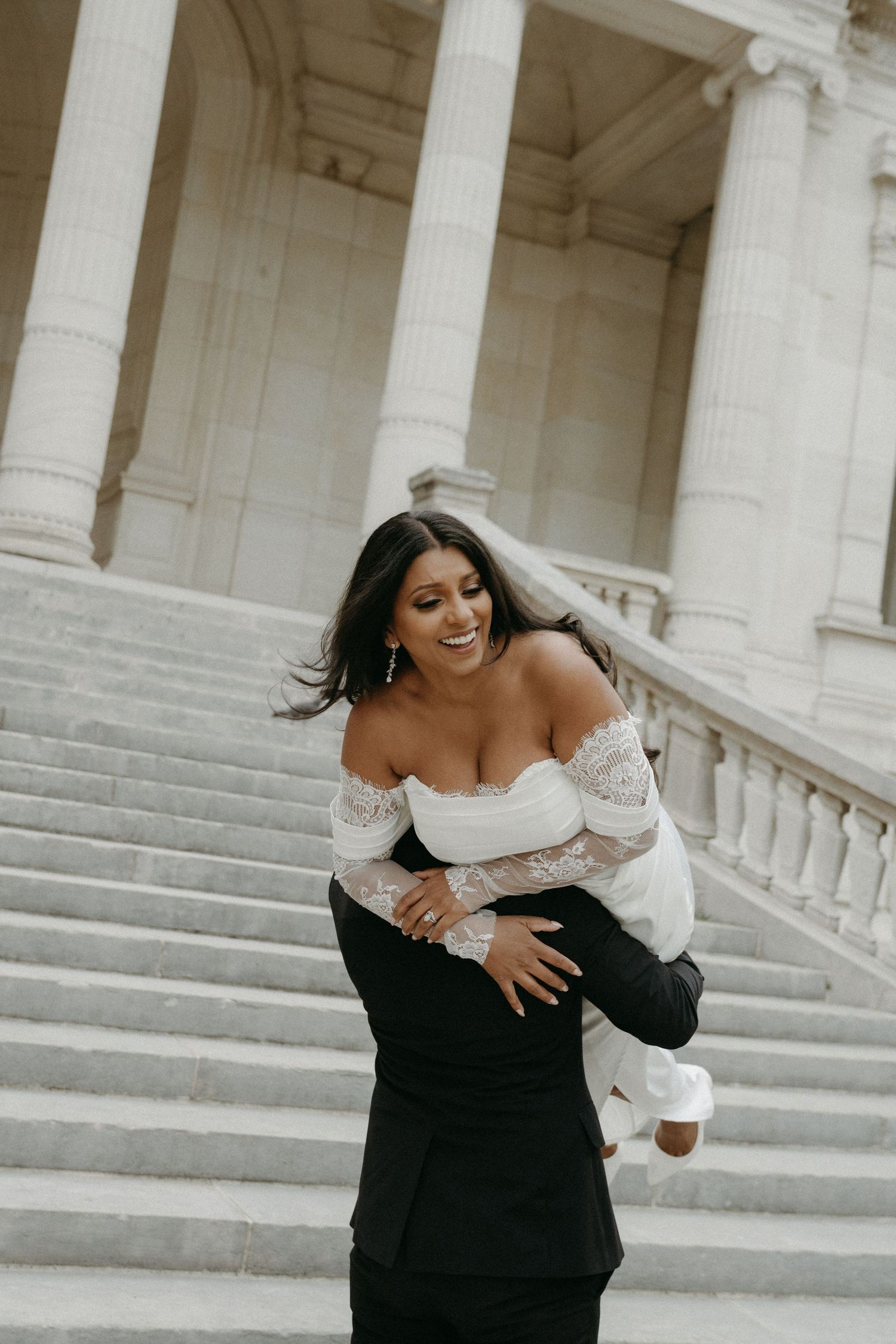 Editorial wedding bride laughing at Palais Galliera in Paris, playful moment on steps, romantic destination photography by Studio Reverie.