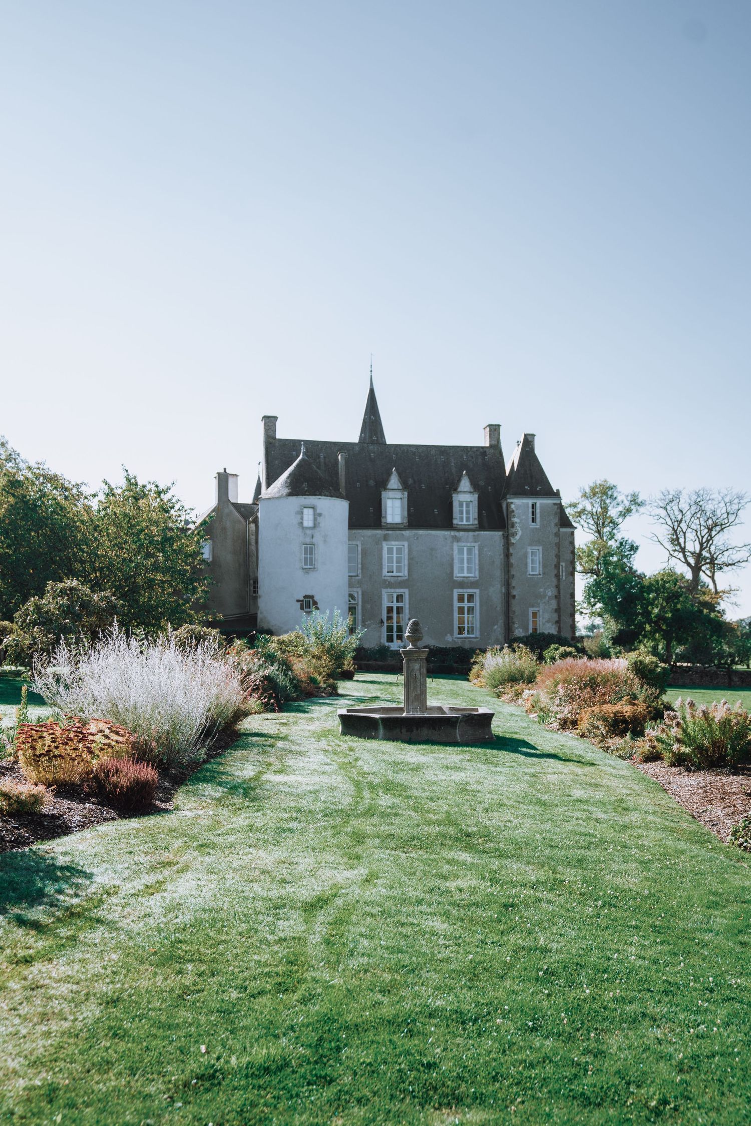 Elegant French chateau with manicured gardens and central fountain surrounded by blooming flowers.