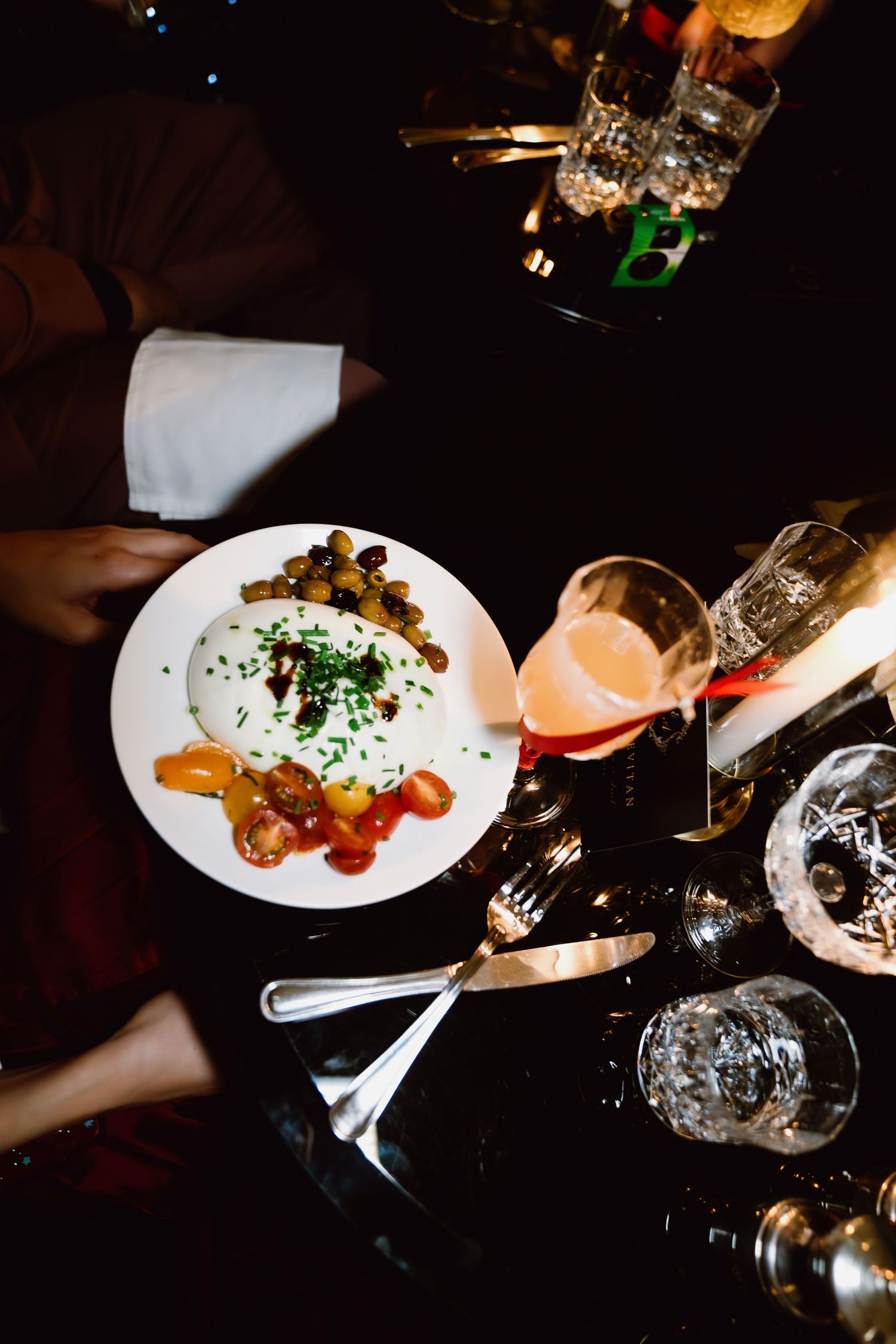 Plated gourmet dishes served in dark ambient restaurant lighting with wine glasses visible.