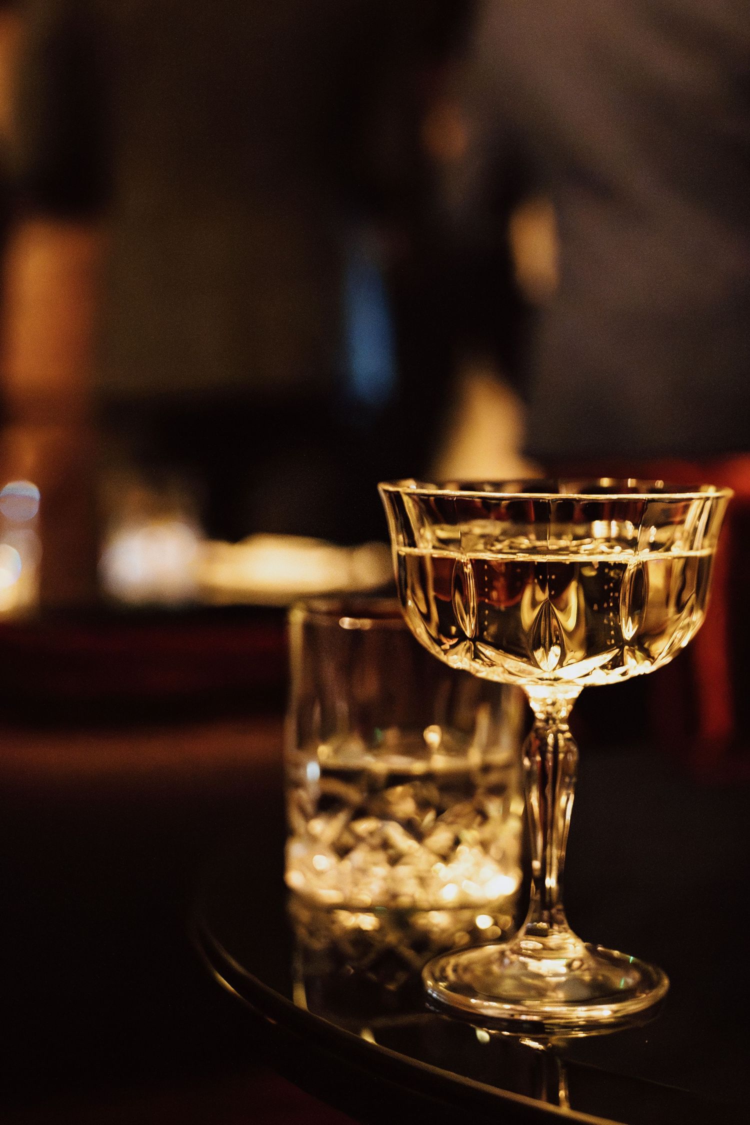 Crystal glasses catch the warm glow of ambient lighting in a dimly lit bar setting.