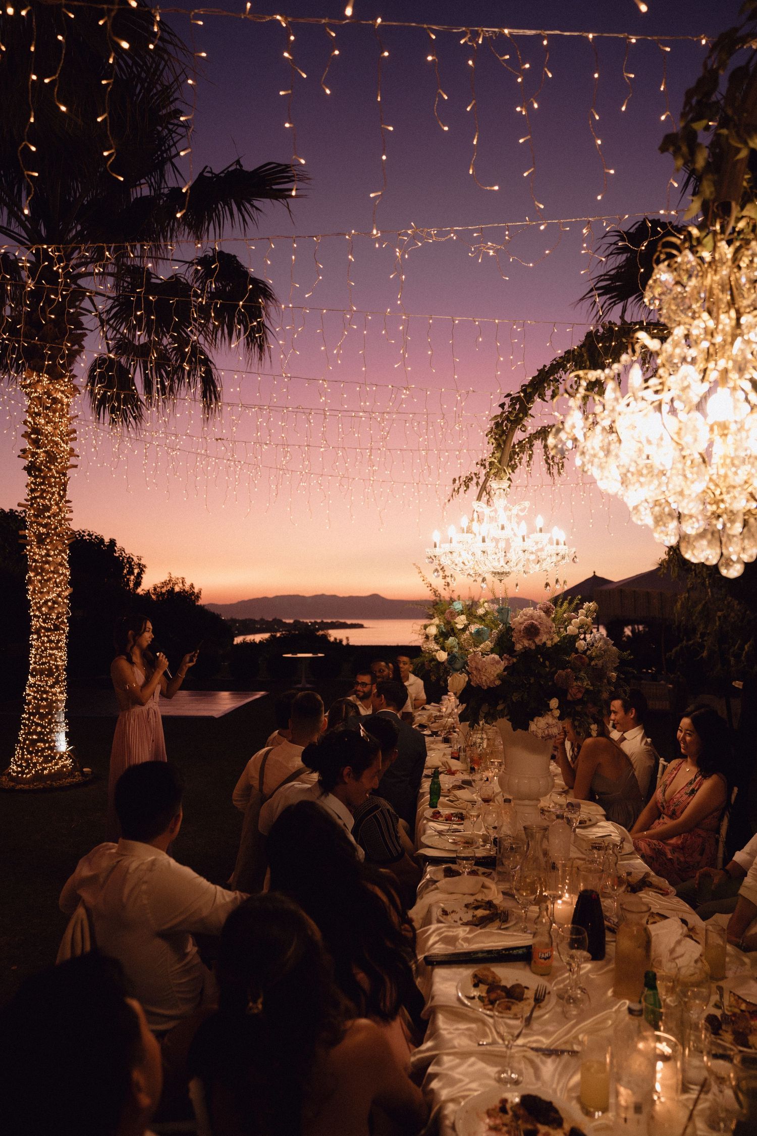 Elegant outdoor wedding reception at sunset with string lights and palm trees creating a magical ambiance.