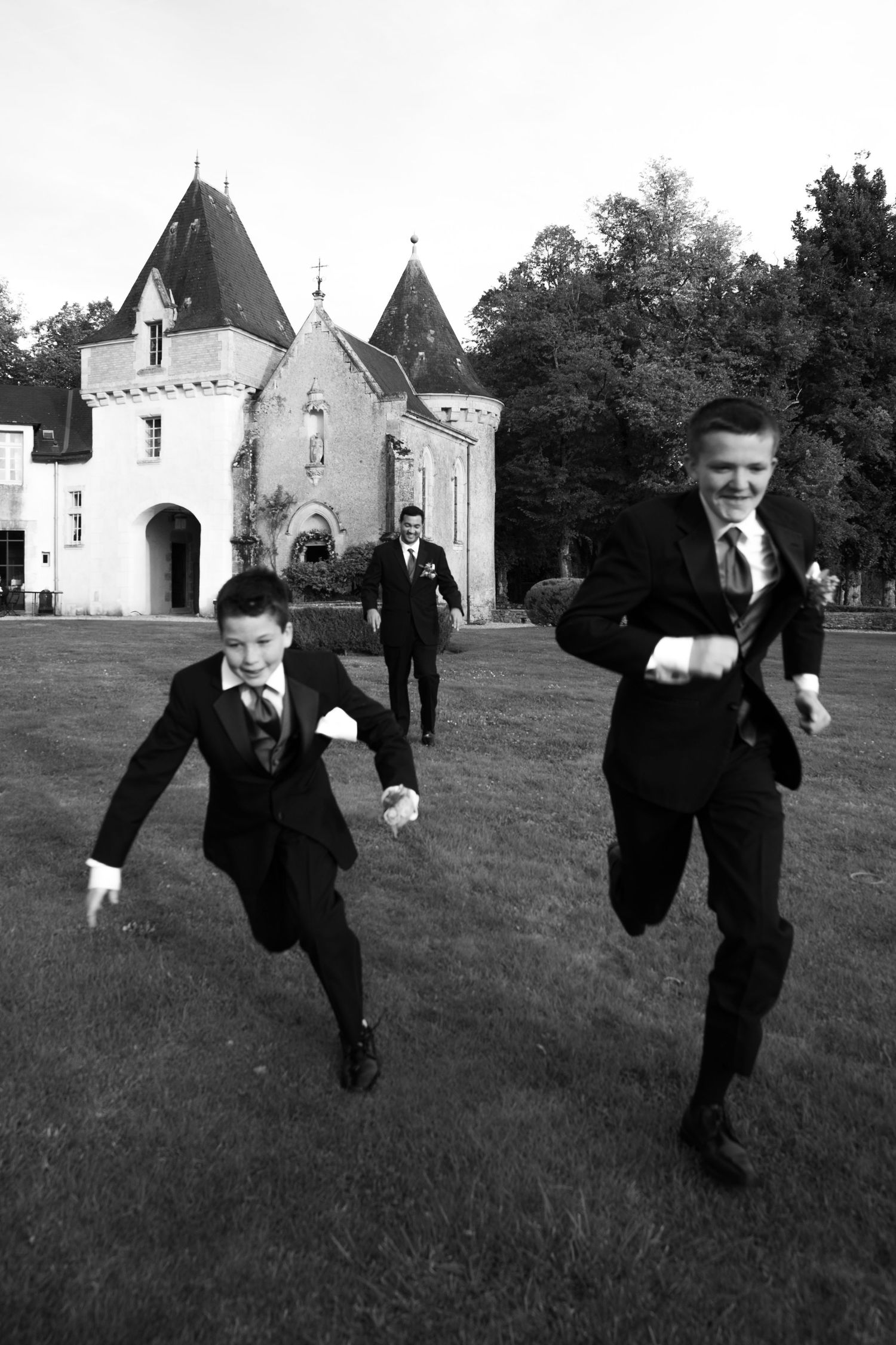 Groomsmen running across lawn at château wedding near Paris, playful and candid destination photography by Studio Reverie.
