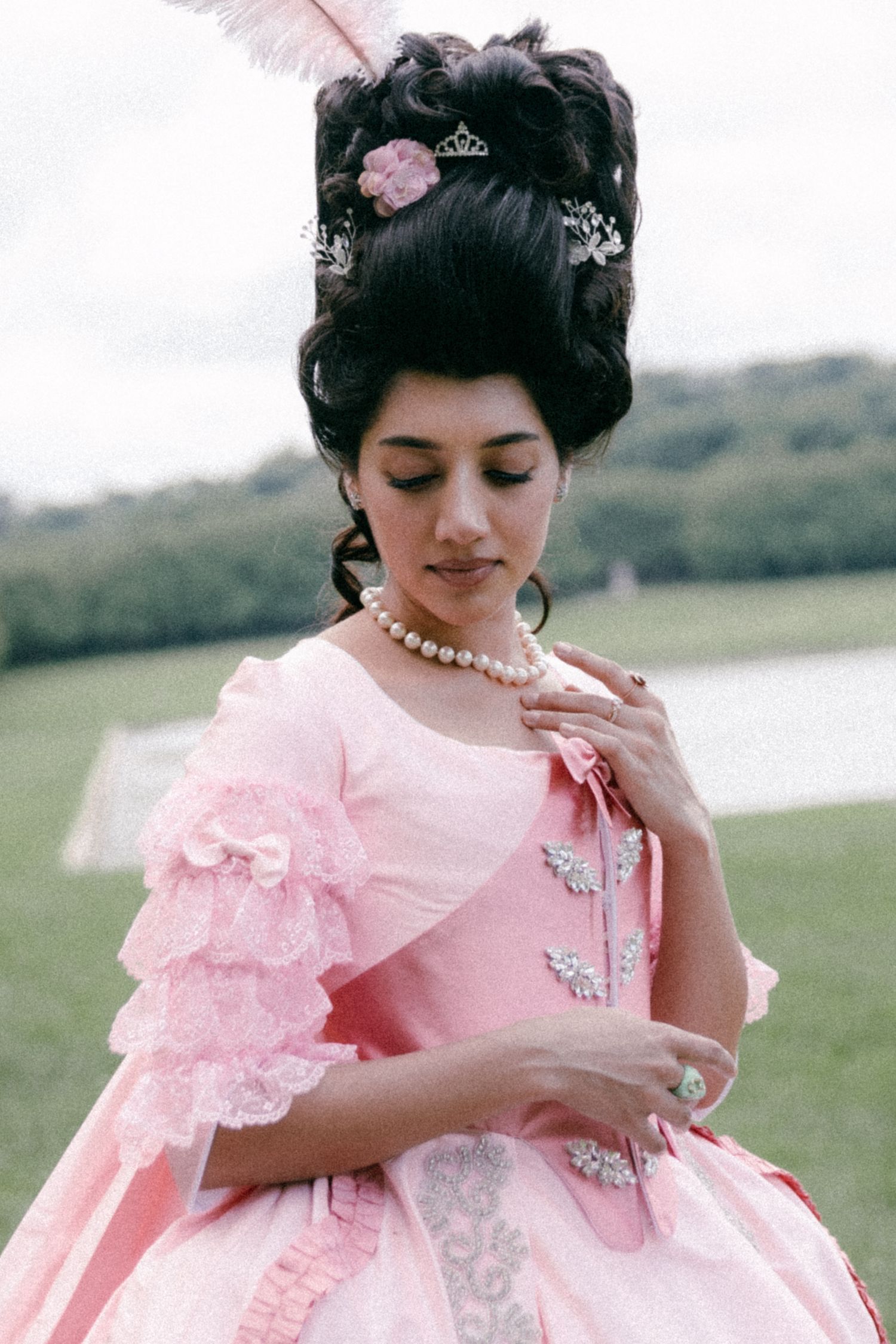A person in a pink Marie Antoinette style dress with ruffled sleeves and an ornate updo hairstyle poses outdoors.