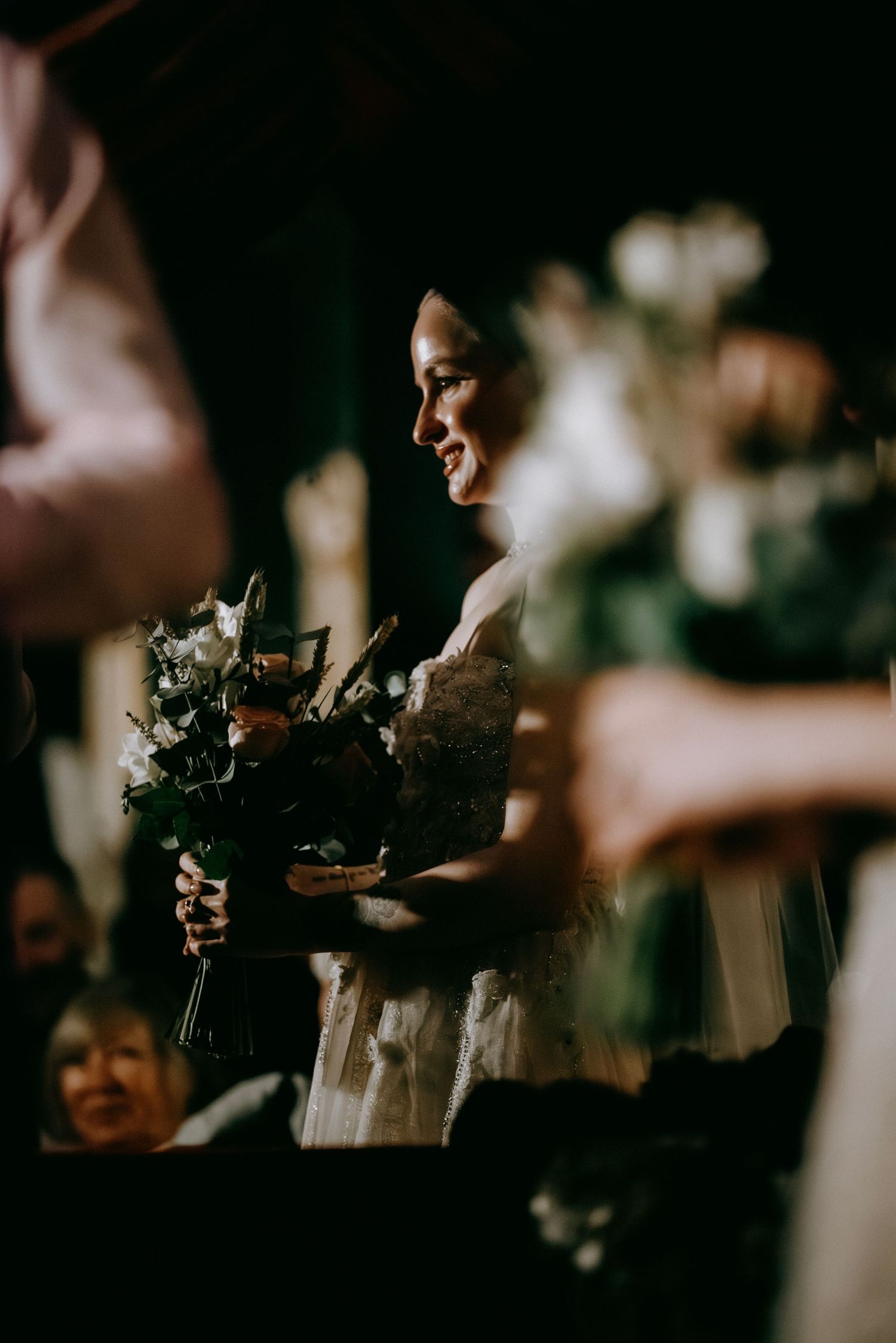 Dark and moody wedding ceremony scene with silhouettes holding flowers.
