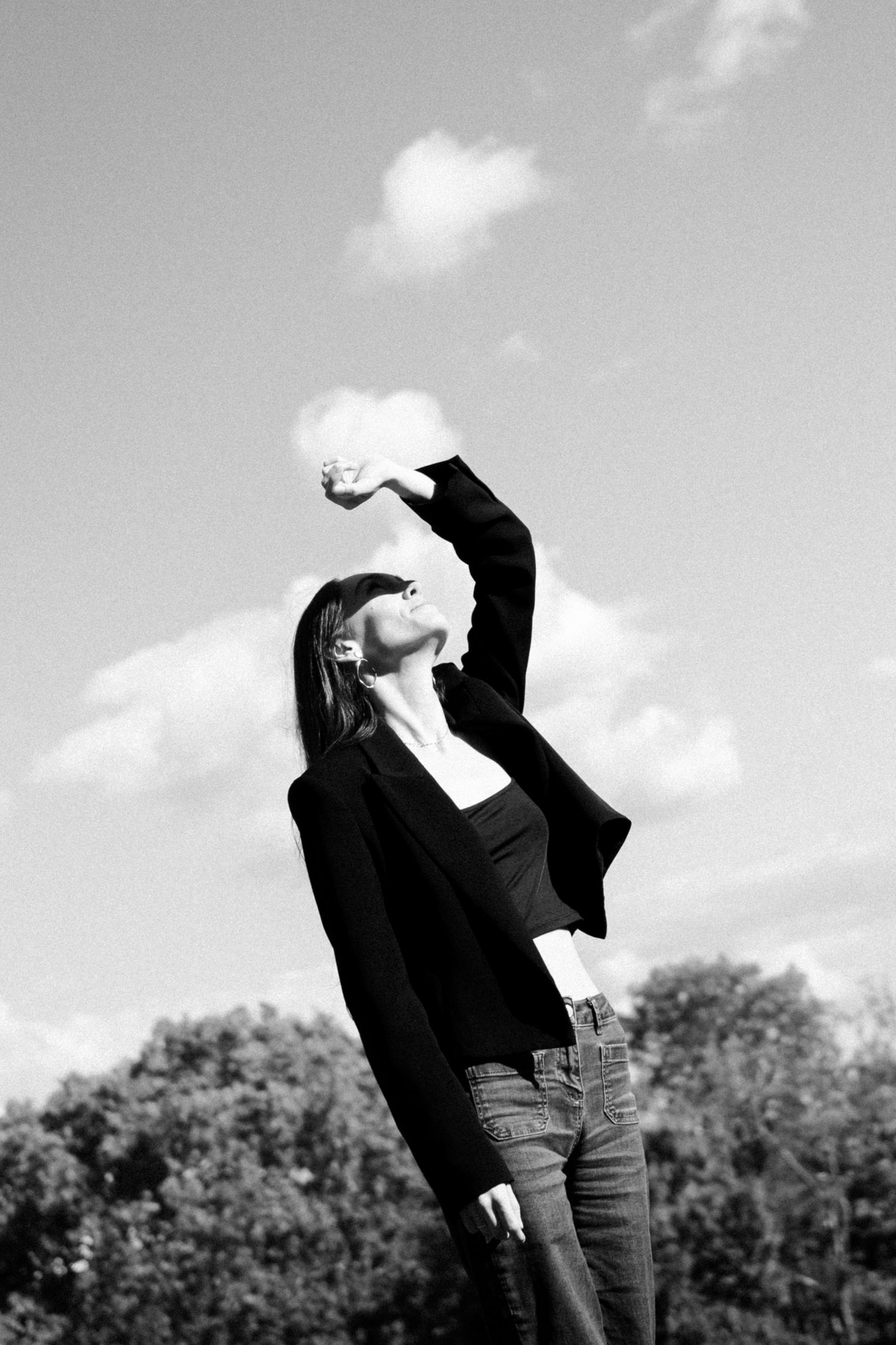 Artistic black and white photography showing a singer keeping the sun from their eyes in a bright sky with clouds.