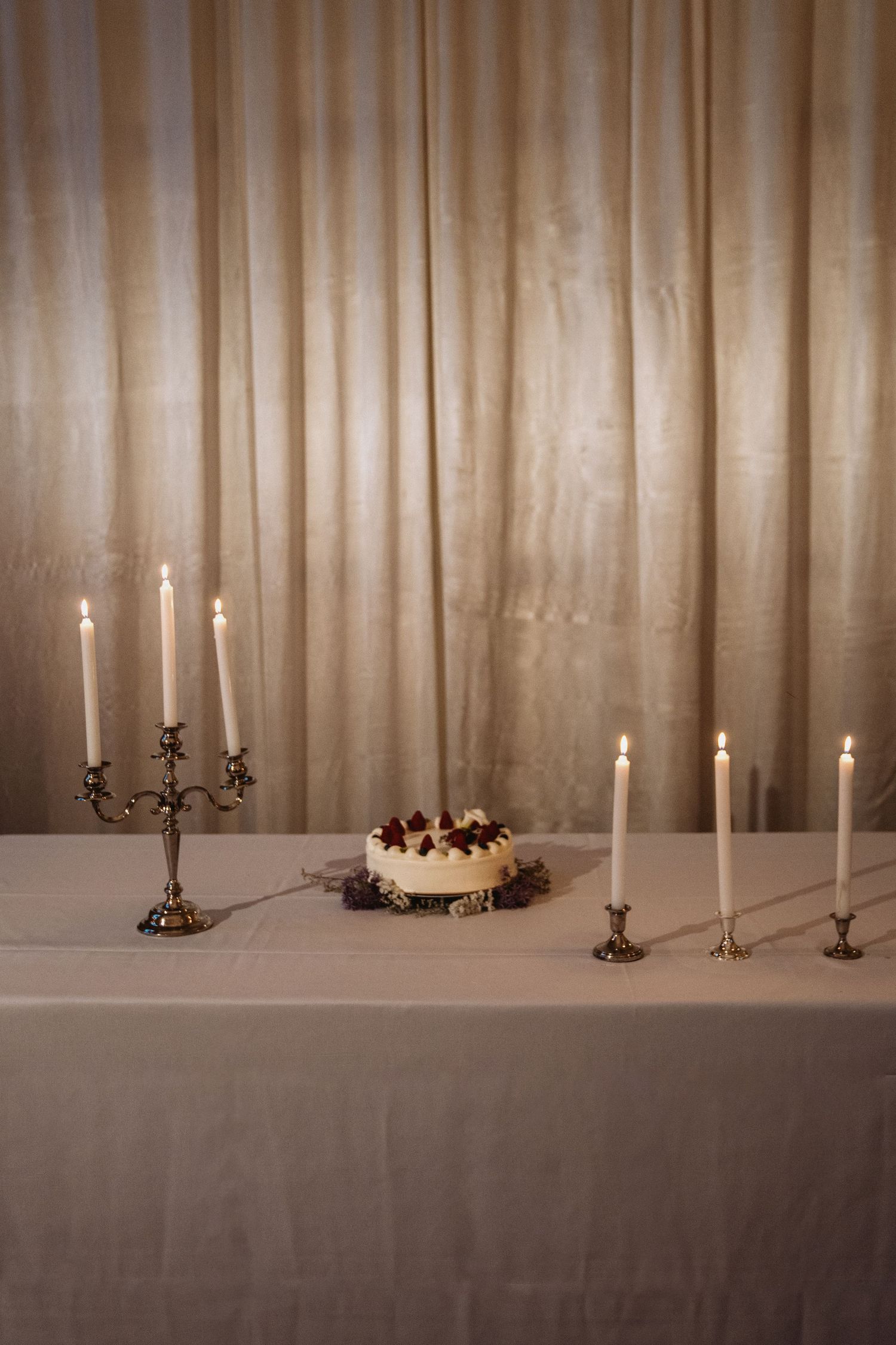 Elegant candlelit table setting with white curtain backdrop and decorative candelabras.