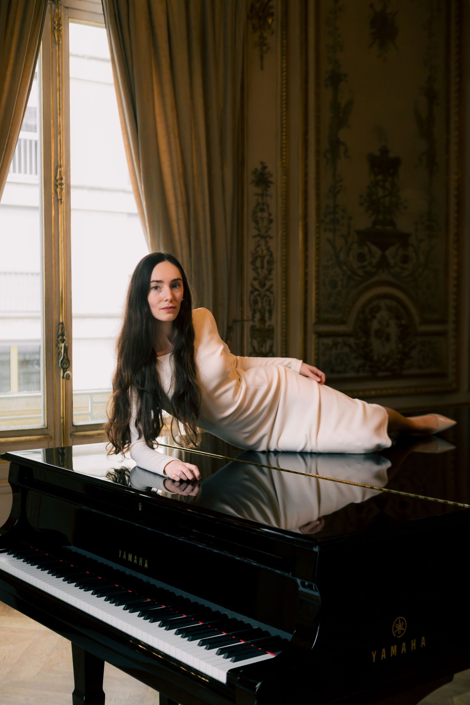 Editorial-style portrait in Paris, woman in white dress reclined on a black grand piano, soft and cinematic