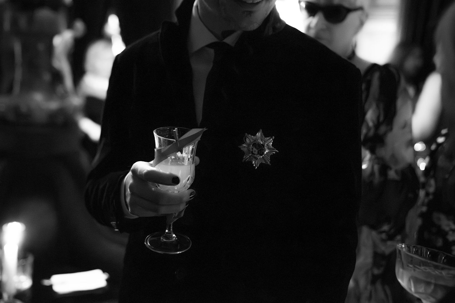 Dimly lit reception scene with formal attire and champagne glasses.