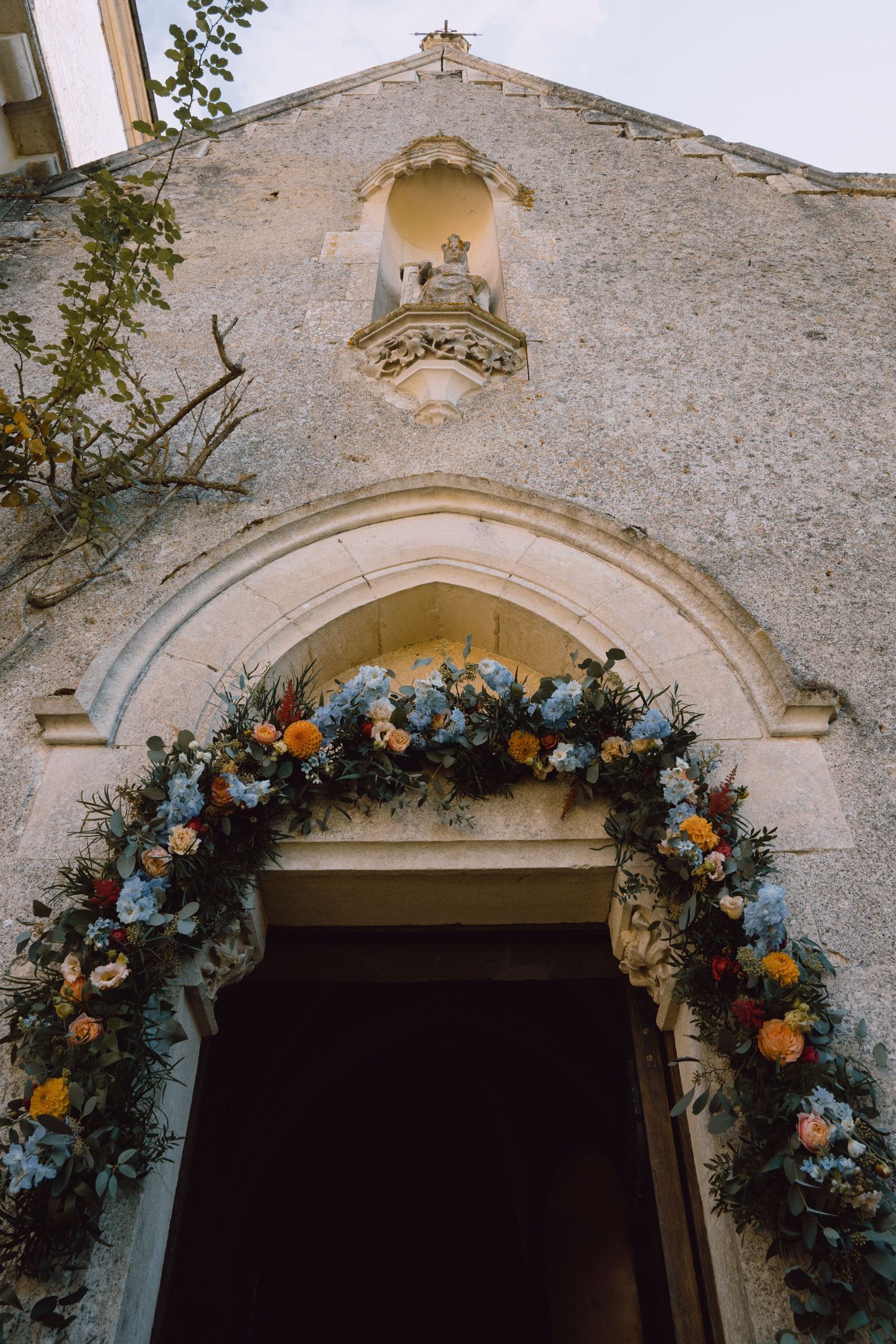 Stone archway entrance decorated with lush floral garland featuring blue and orange blooms.