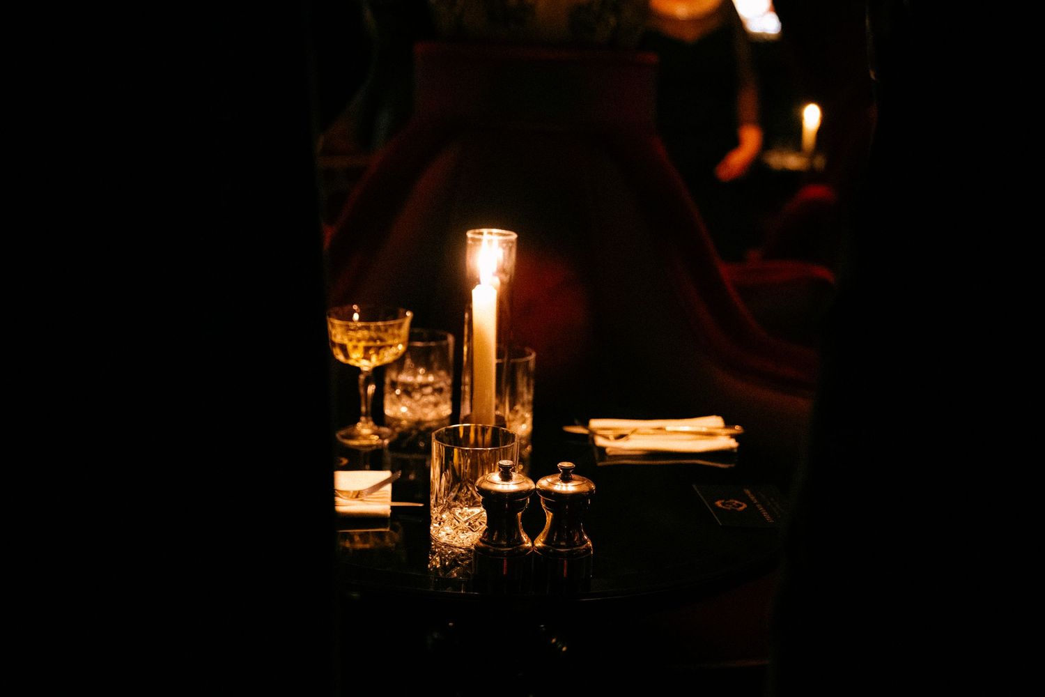 Glowing candlelight illuminates wine glasses and table settings in a dimly lit romantic restaurant atmosphere.