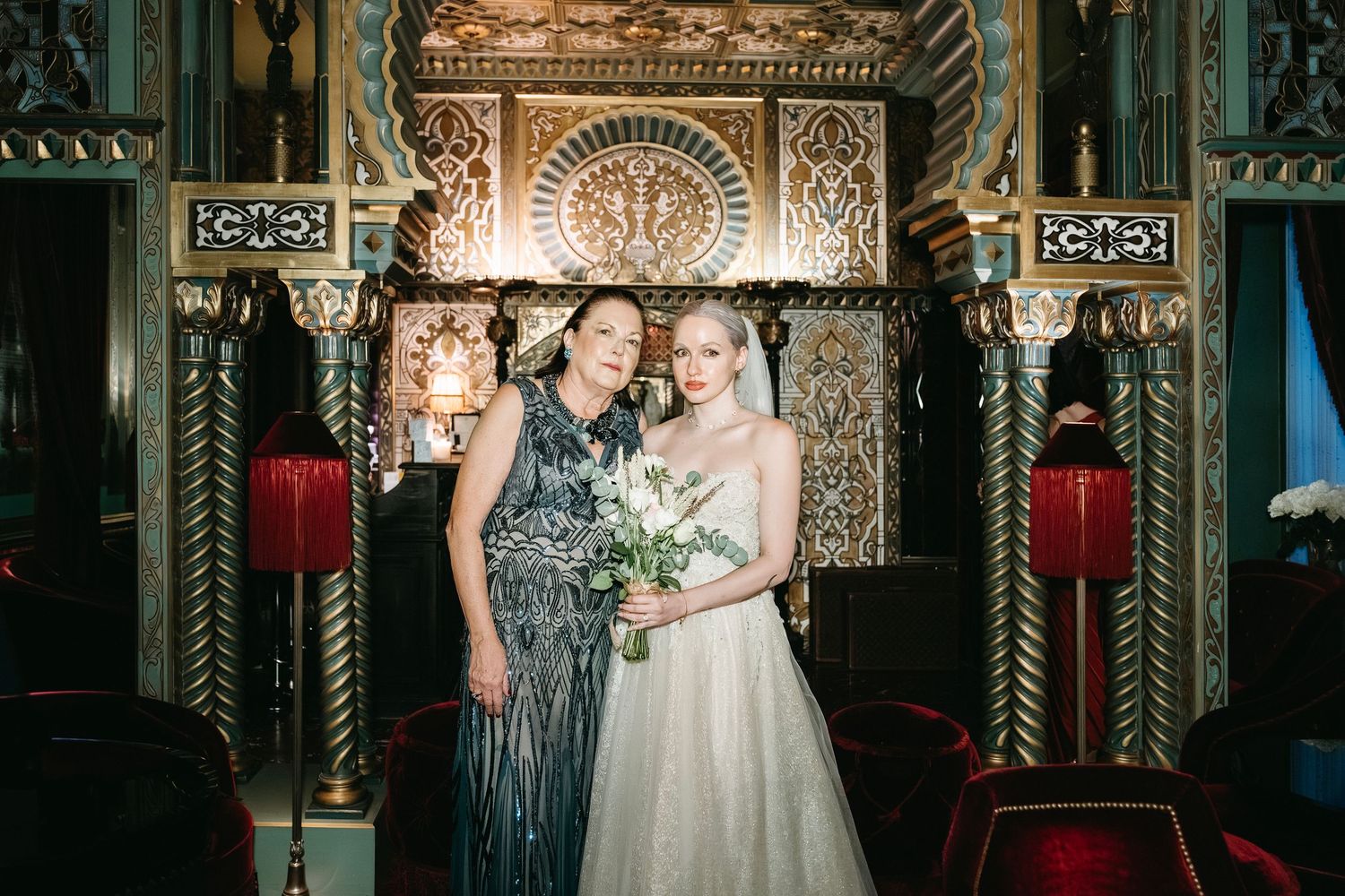 A couple shares an intimate moment under ornate architectural details in a dimly lit historic venue during their wedding.