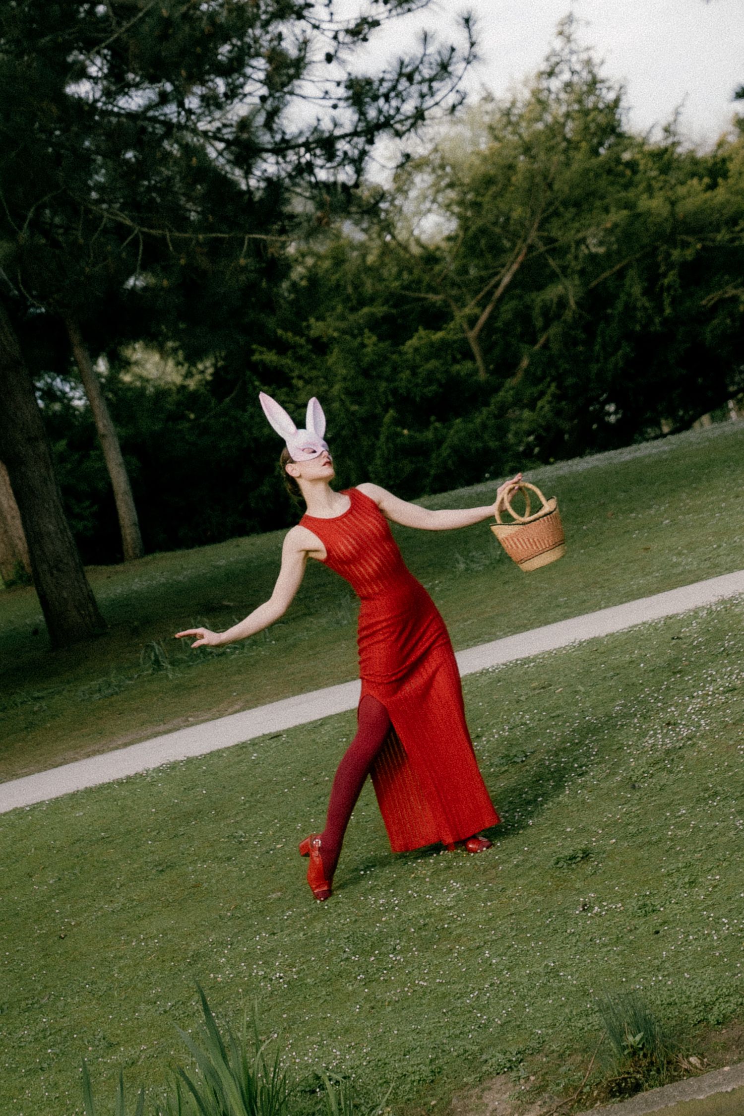 Paris editorial shoot in nature, model in red gown and rabbit mask walking with basket, playful and surreal concept. By Studio Reverie