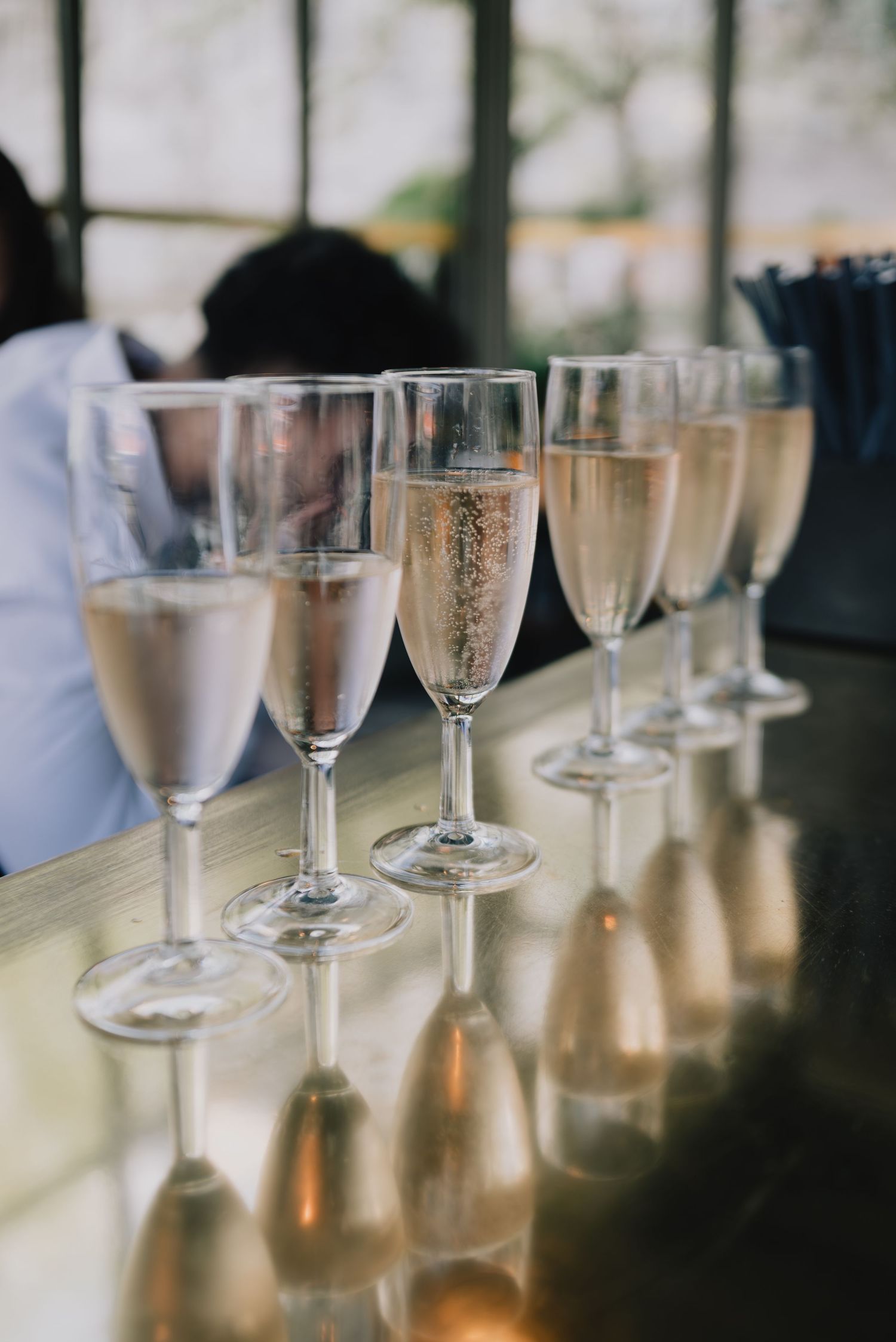 A row of elegant champagne glasses filled with sparkling wine sit on a table casting reflective shadows.