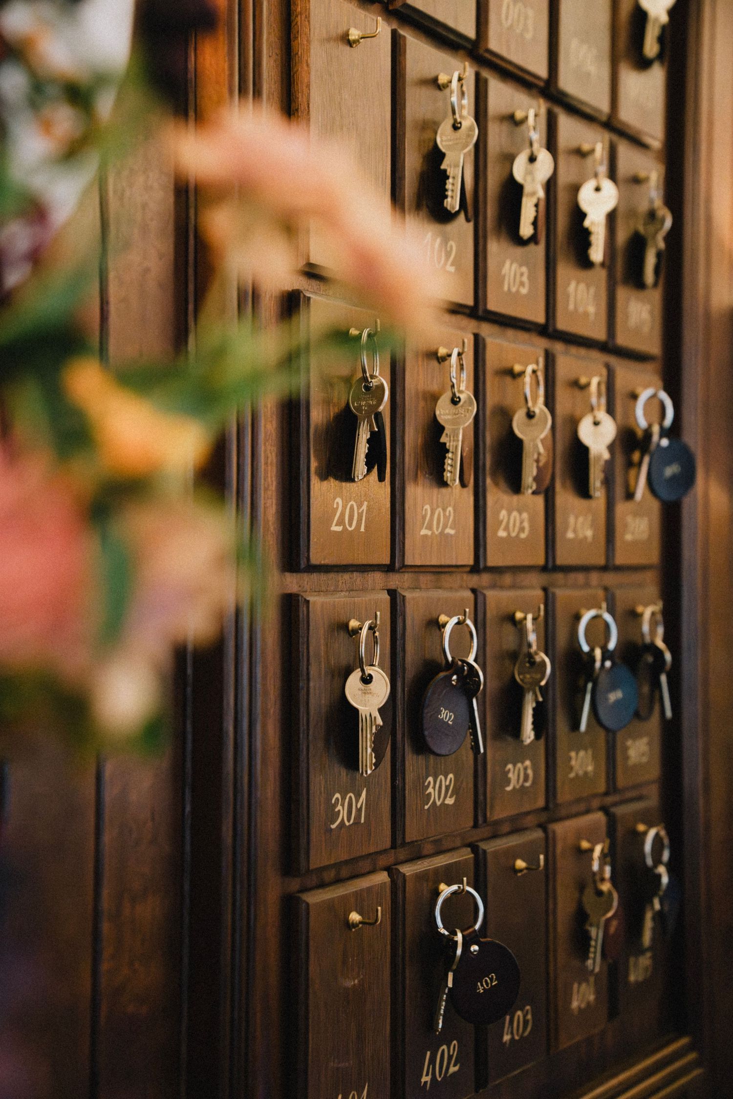 Vintage wooden post office boxes with numbered brass doors and antique keys hanging from keyholes in dim lighting.