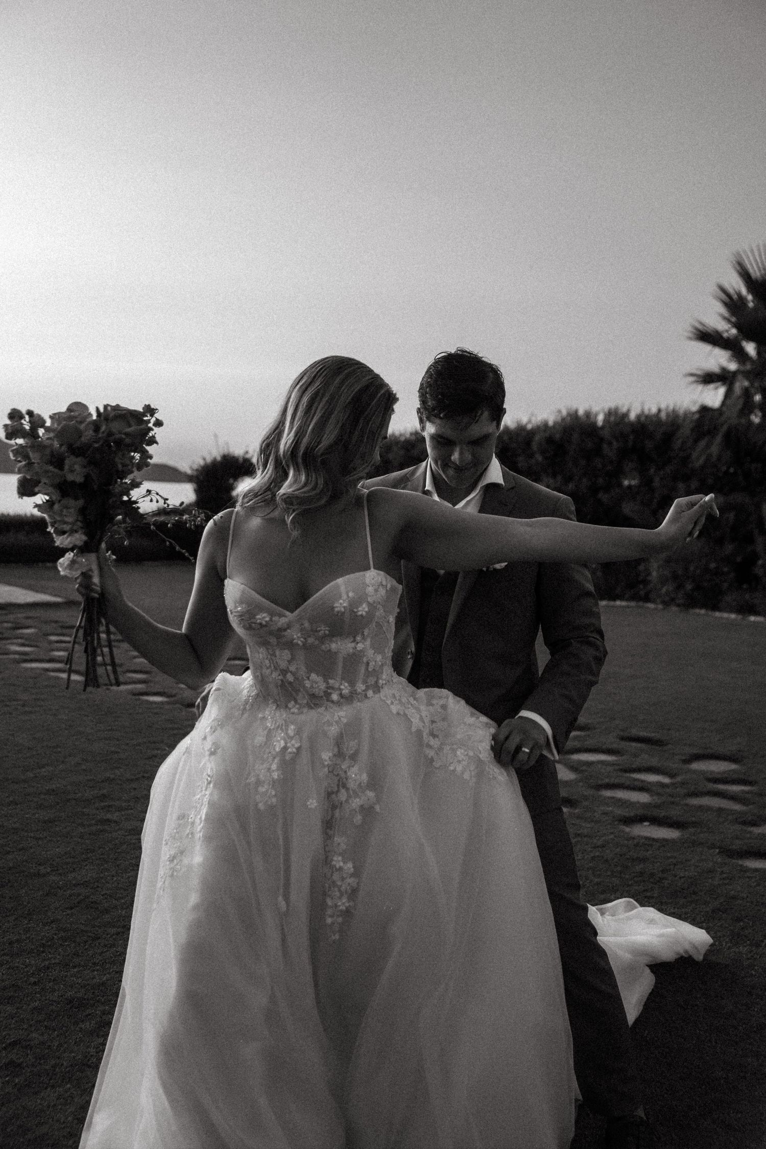 A couple dances together at sunset on a golf course with palm trees in the background.