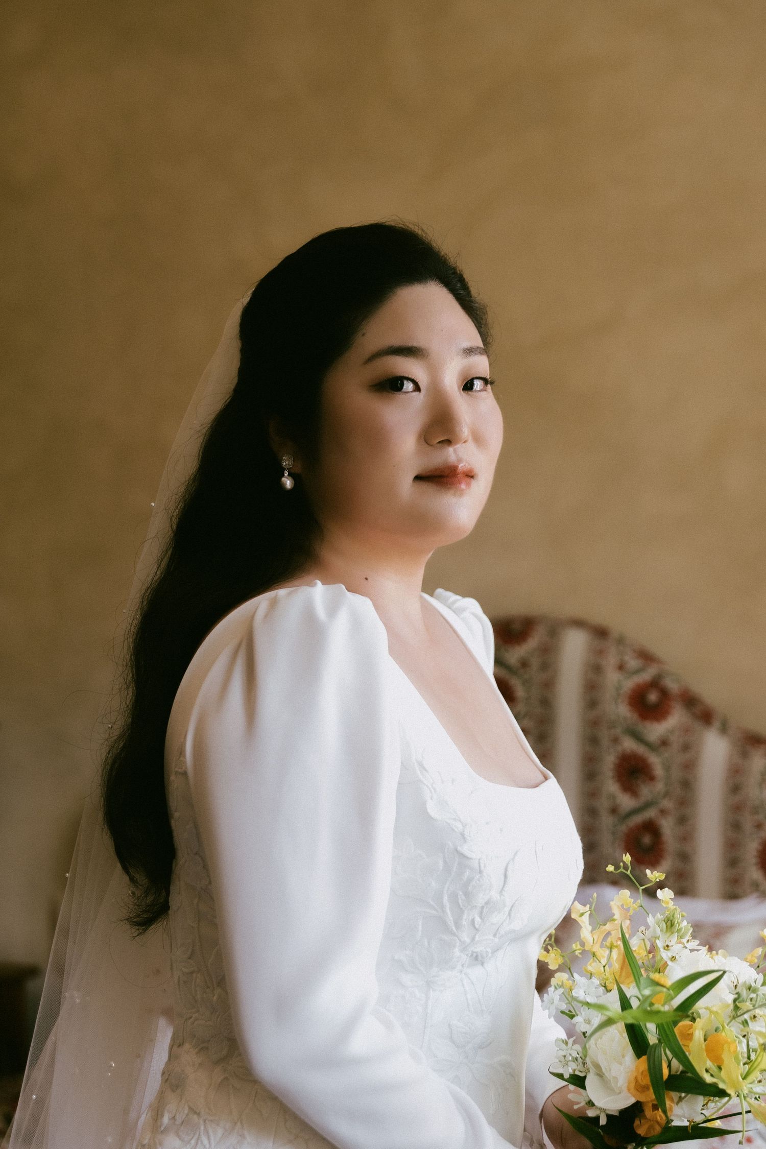 Elegant bridal portrait featuring a white long-sleeved wedding dress and yellow lily bouquet.