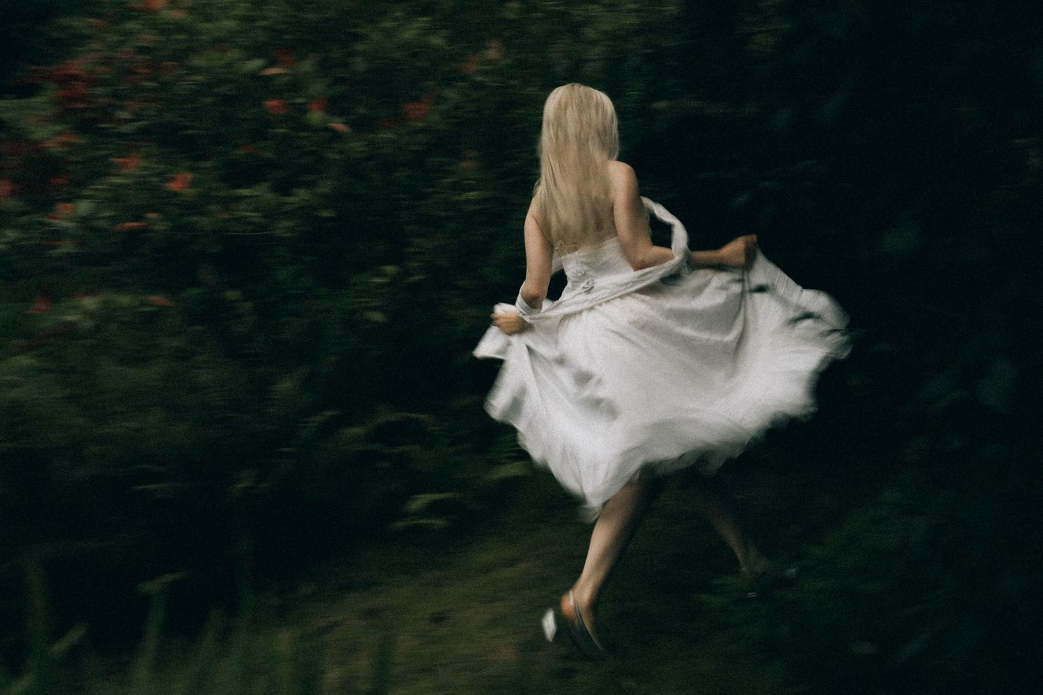 A blonde woman in a flowing white dress running through a lush green garden.