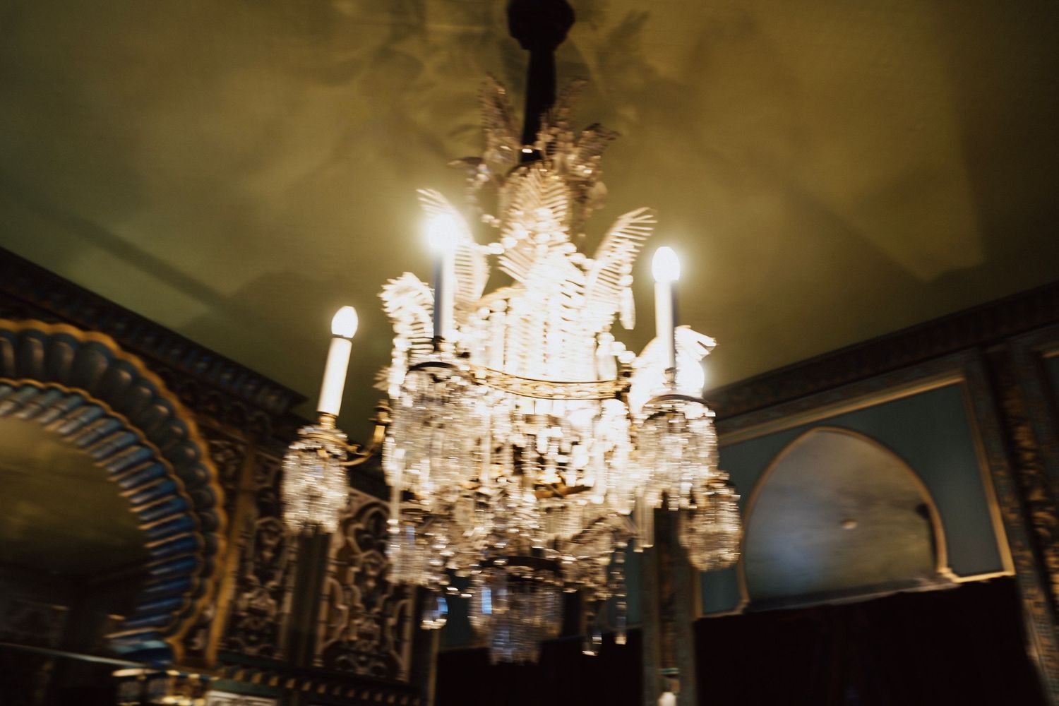 Crystal chandeliers hang from ornate ceilings in an elegant ballroom with classical architectural details.