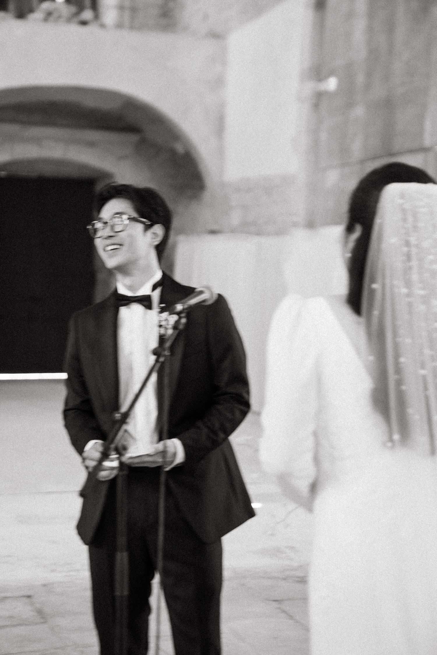 Wedding couple in formal attire sharing a joyful moment in an elegant archway setting.