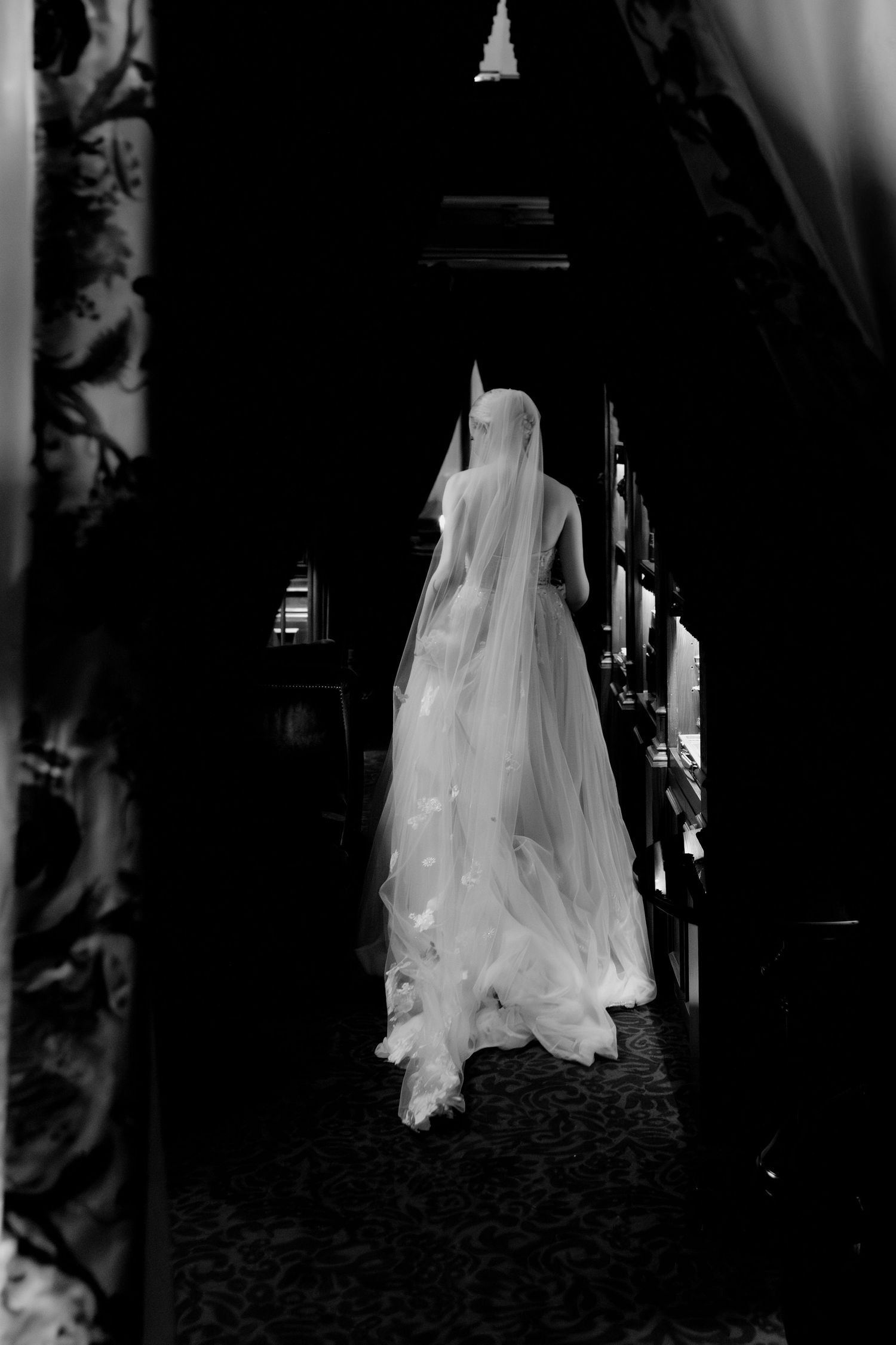 Flowing white wedding dress captured in dramatic shadows along a dark hallway.