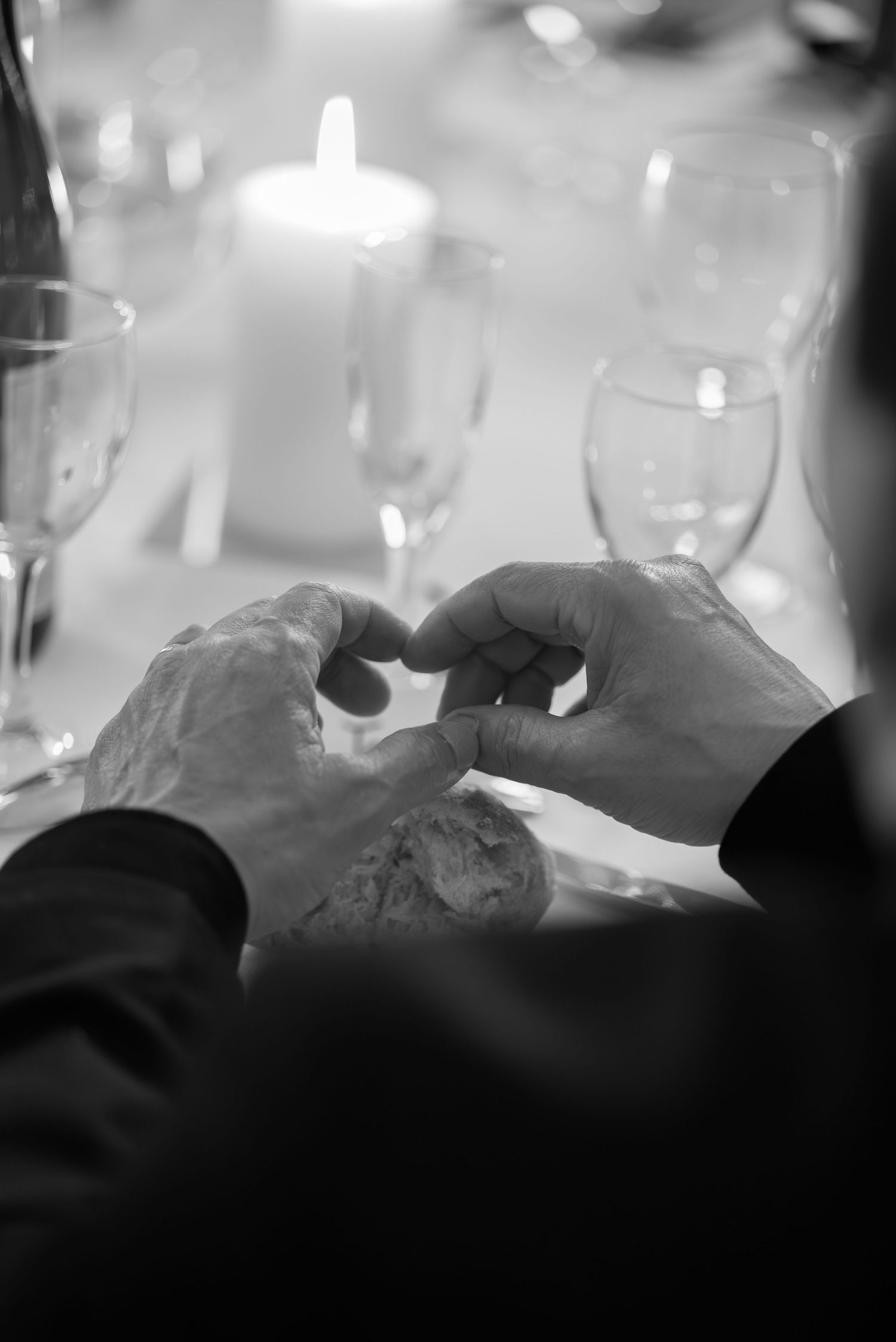 Black and white image of wine glasses arranged on a table with soft bokeh lighting effects.