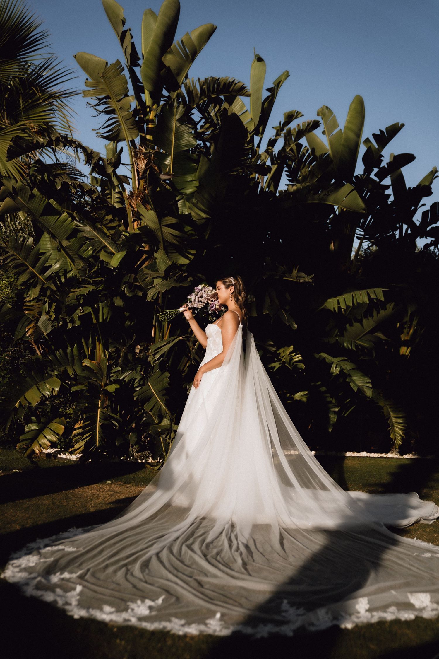 Dramatic bridal portrait with flowing white dress against tropical palm trees and natural lighting.