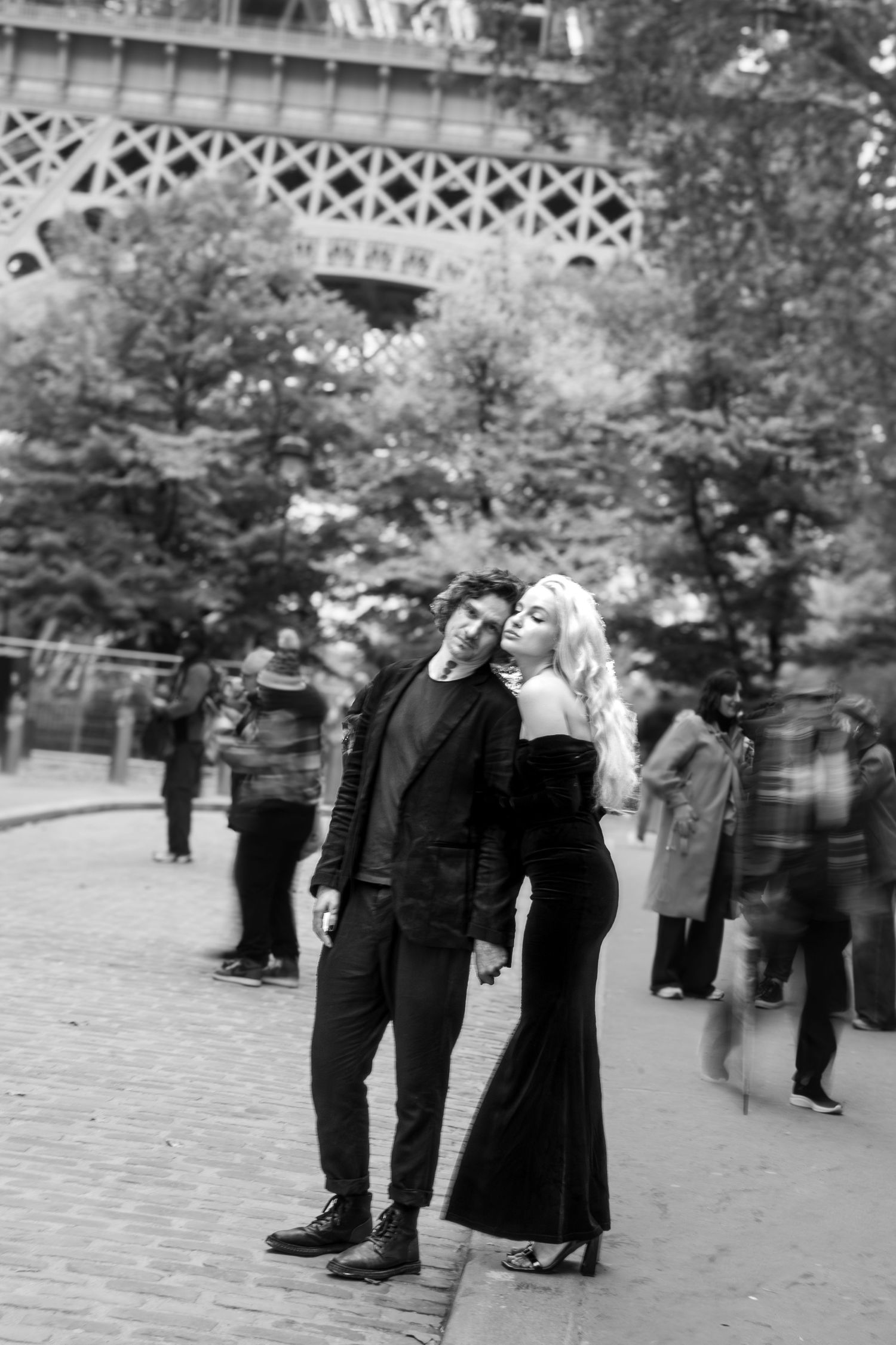 Cinematic couple moment under the Eiffel Tower in Paris, captured unposed in elegant black for an editorial-style shoot.