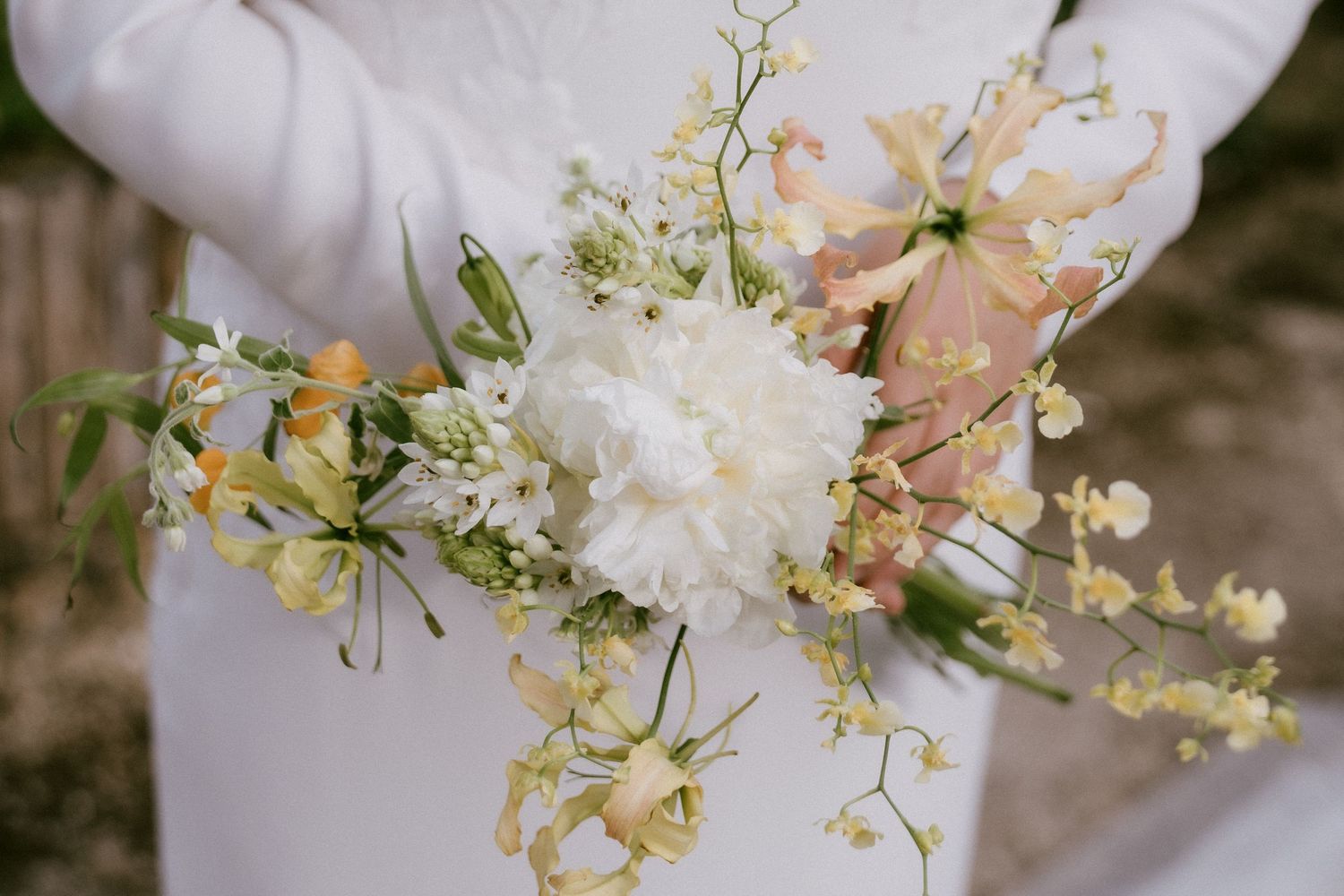 A delicate bridal bouquet featuring white carnations, peach flowers, and baby's breath wrapped in a light blue ribbon.