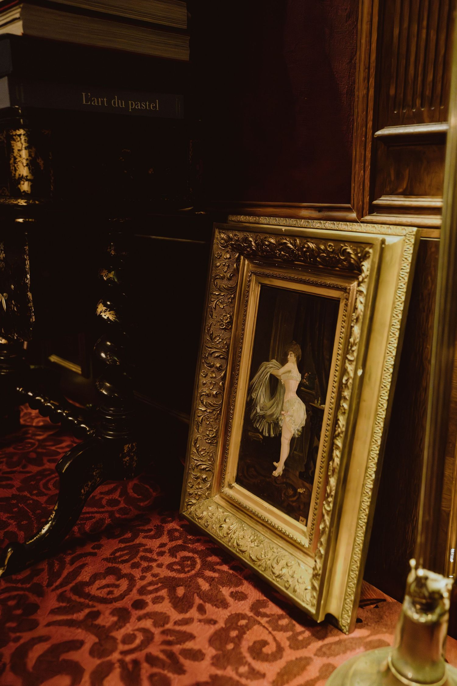 Ornate gold-framed mirrors reflect dim lighting along a hallway with red patterned carpet.