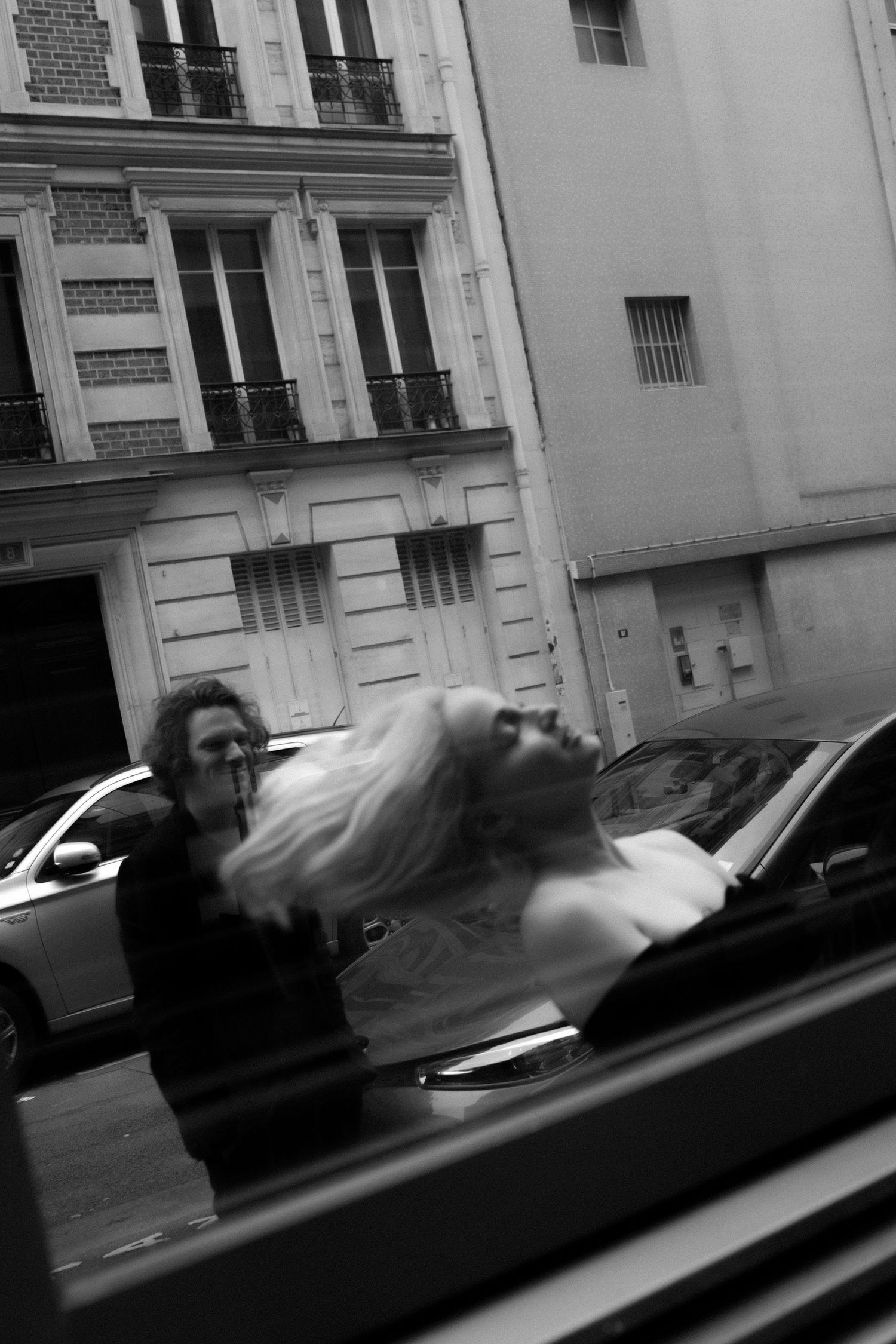 Candid cinematic Paris moment. Black and white photo of woman whipping her blonde hair, caught in the reflection of a nearby window.