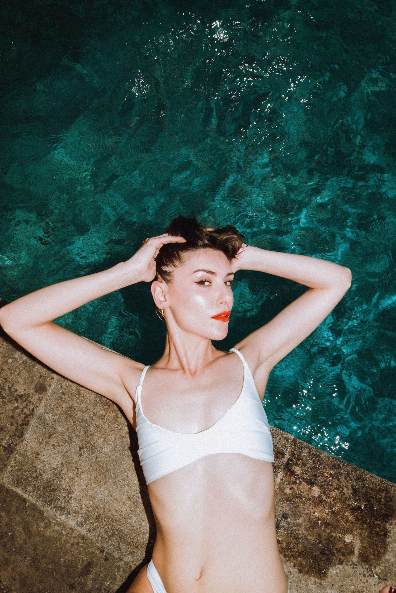 Editorial swimwear shoot in the South of France, model in white bikini top by a turquoise pool, relaxed and luminous. By Studio Reverie.