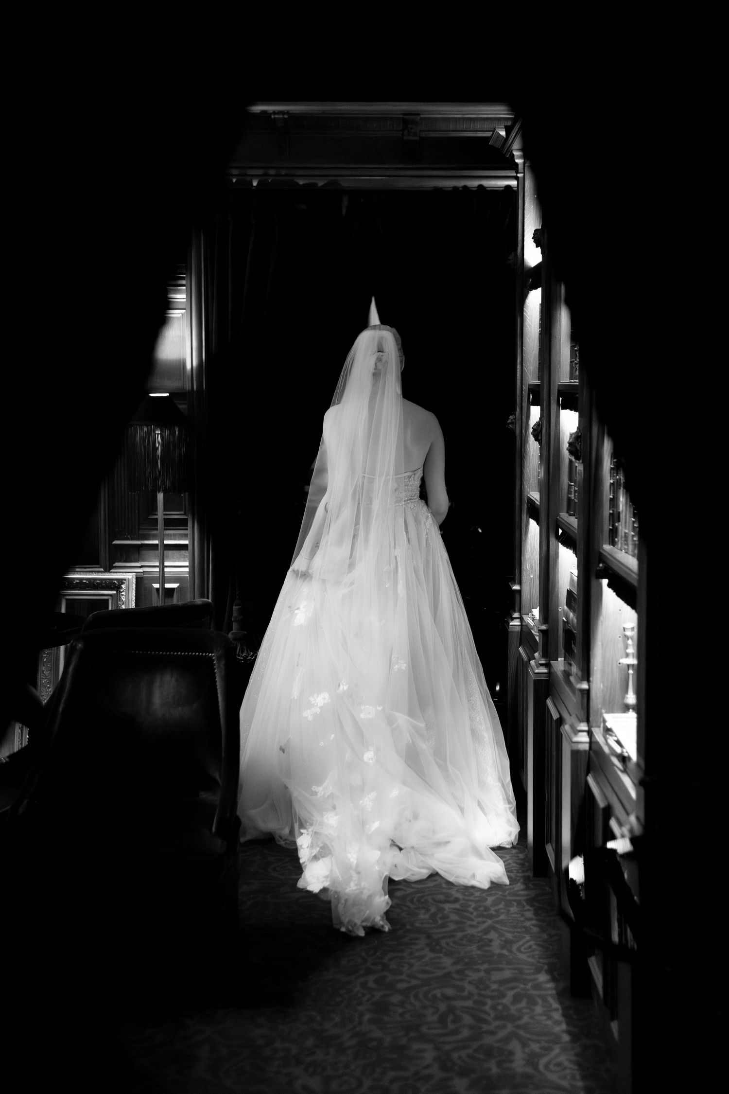 Ethereal white bridal gown glowing against dark hallway in artistic black and white photography.