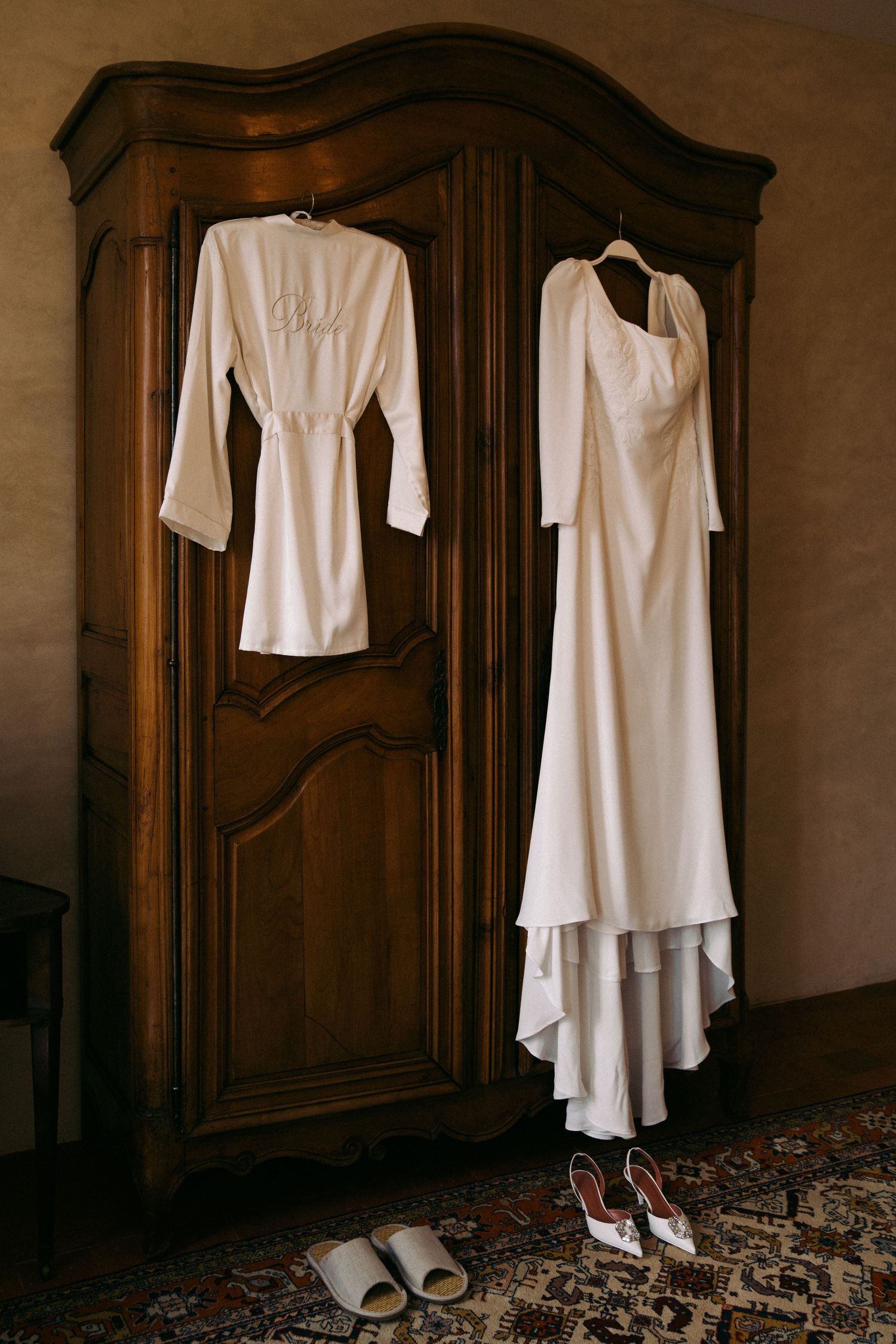 White vintage clothing and dresses displayed hanging against dark wooden armoires in atmospheric lighting.