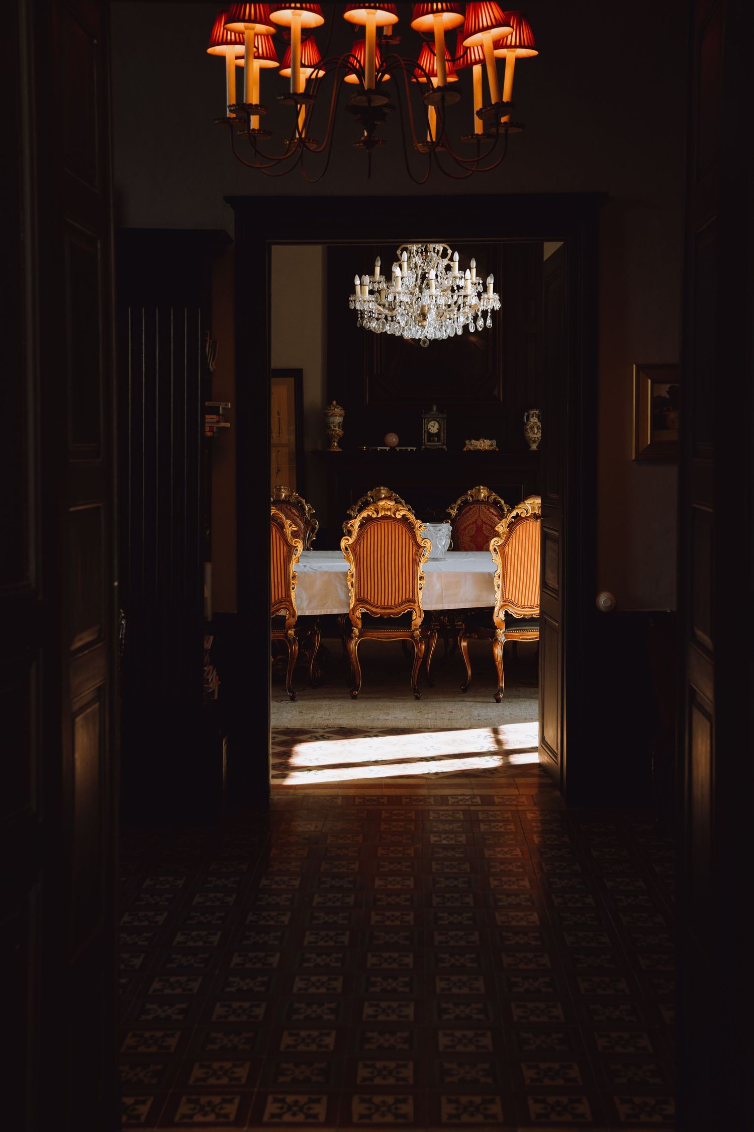 Elegant dining room with crystal chandeliers and ornate chairs illuminated in dramatic lighting.