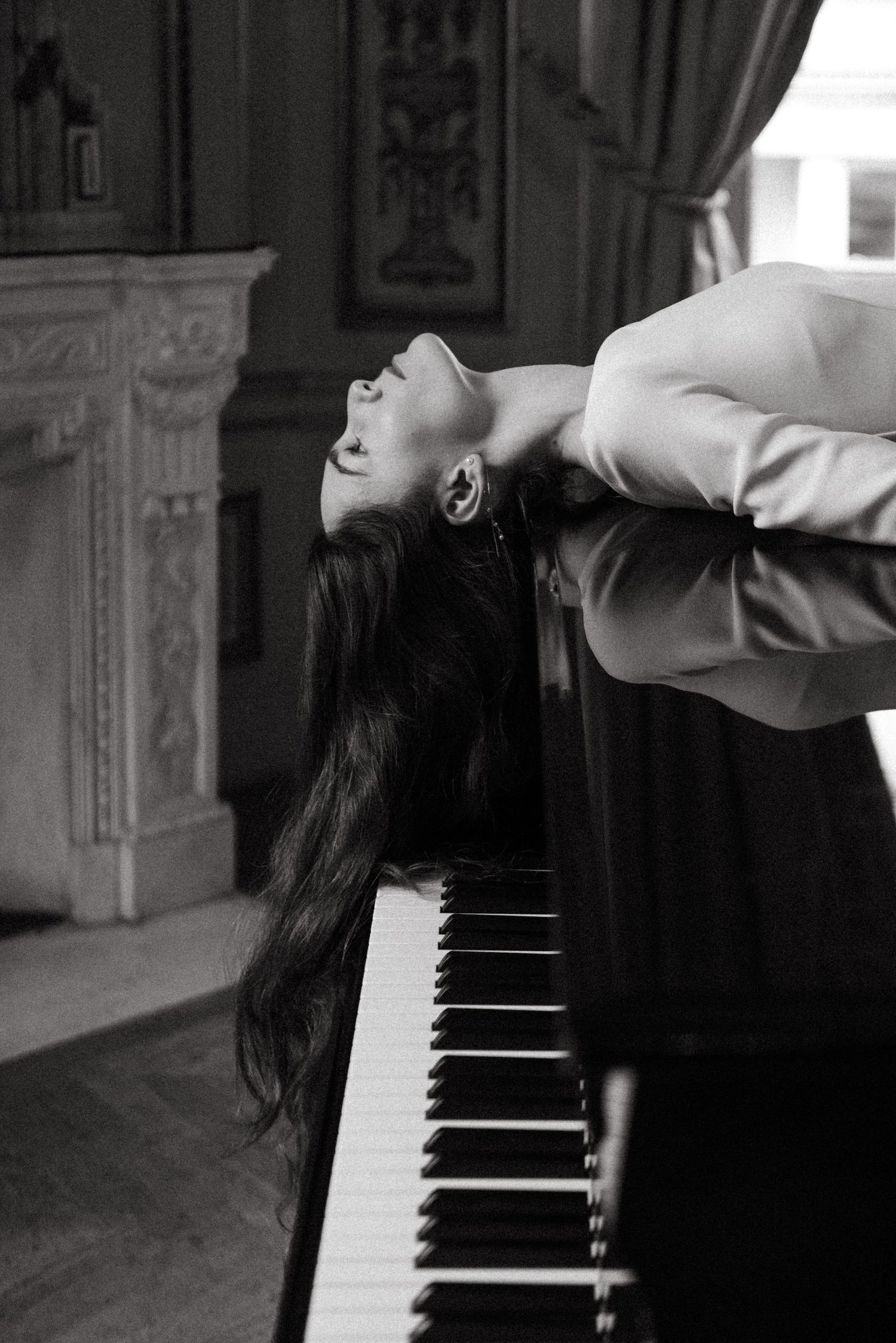 Black and white cinematic portrait in Paris, woman draped across piano in soft light, poetic and stylish. Photography by Studio Reverie.