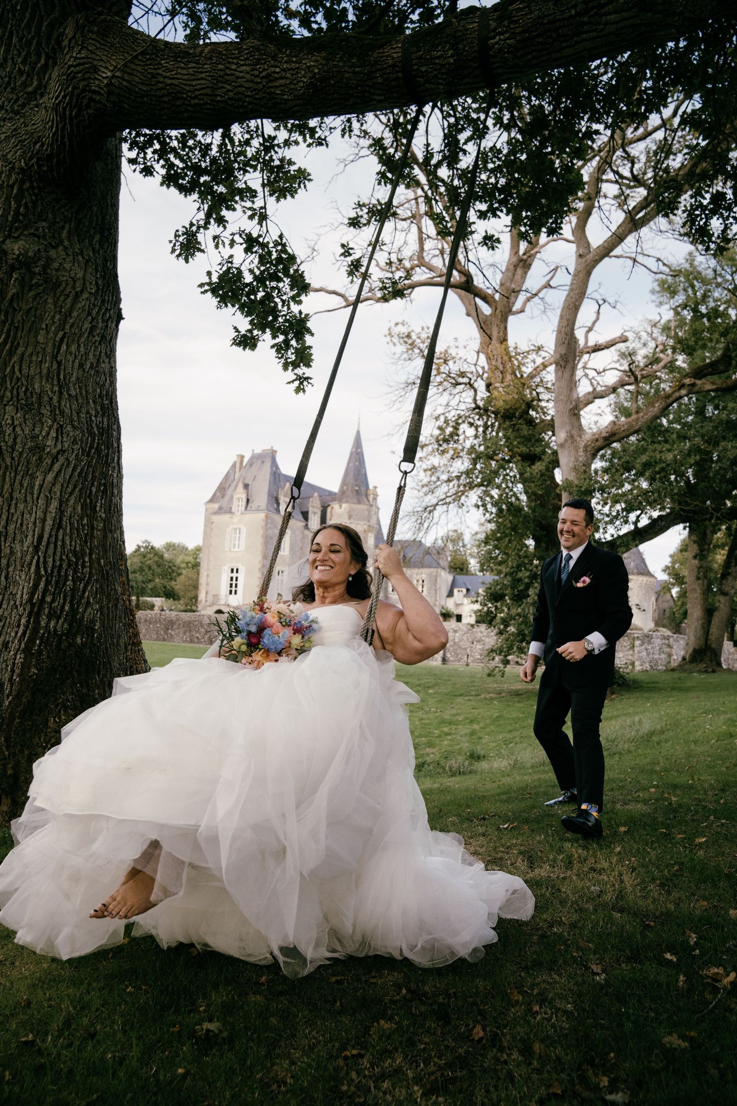 Bride on swing in front of château near Paris, joyful and cinematic destination wedding photography by Studio Reverie.