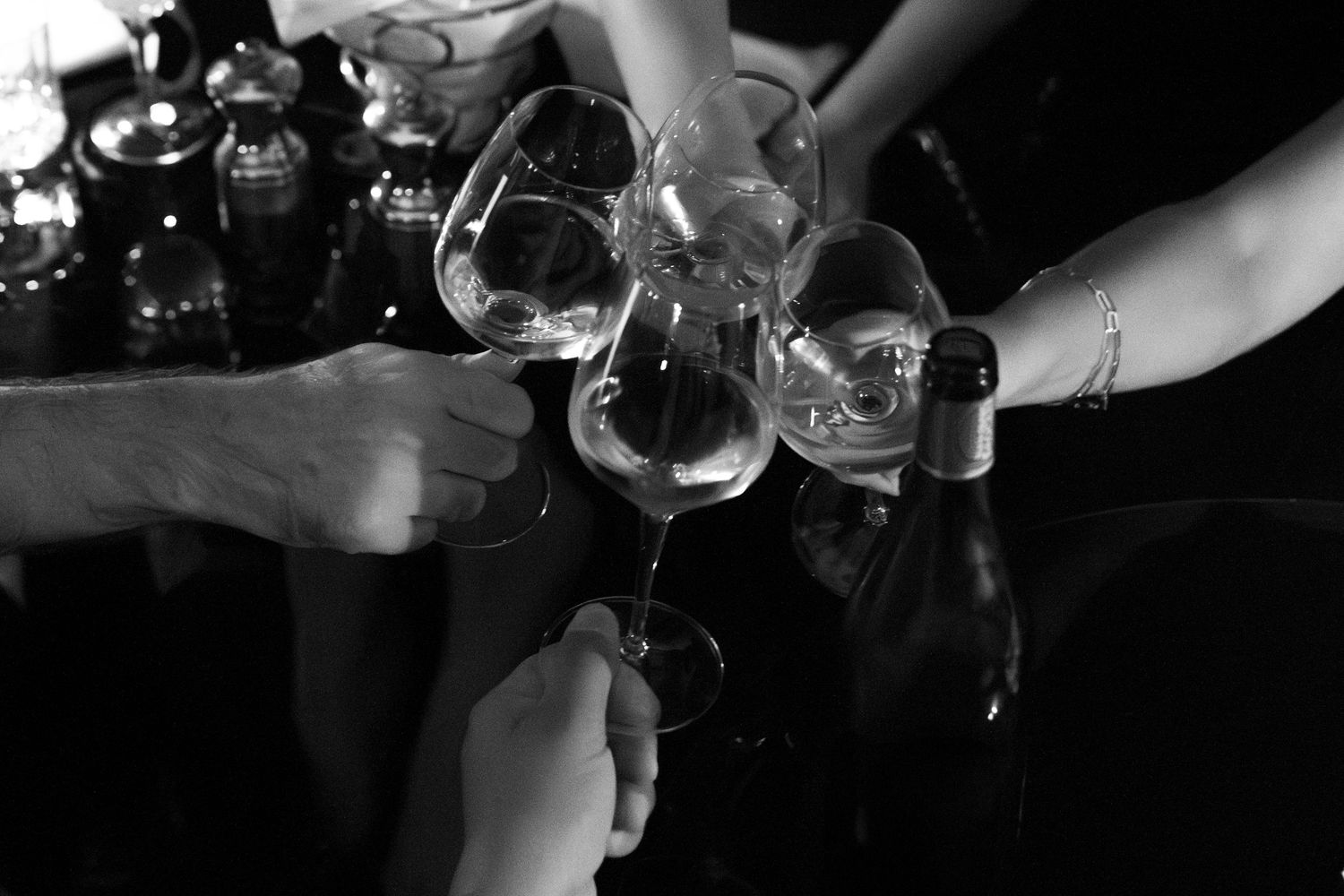 Hands pouring drinks from bottles at a bar in a dimly lit nightclub setting.