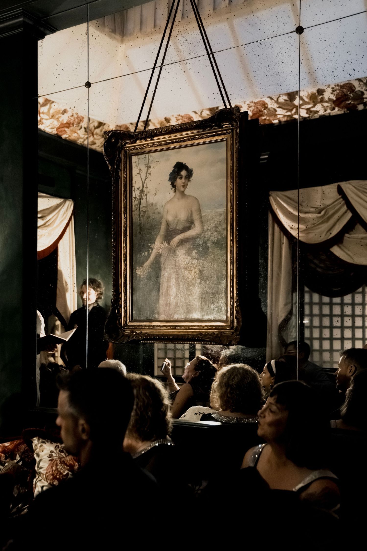 Vintage framed artwork hangs on the wall as guests gather in a dimly lit room.