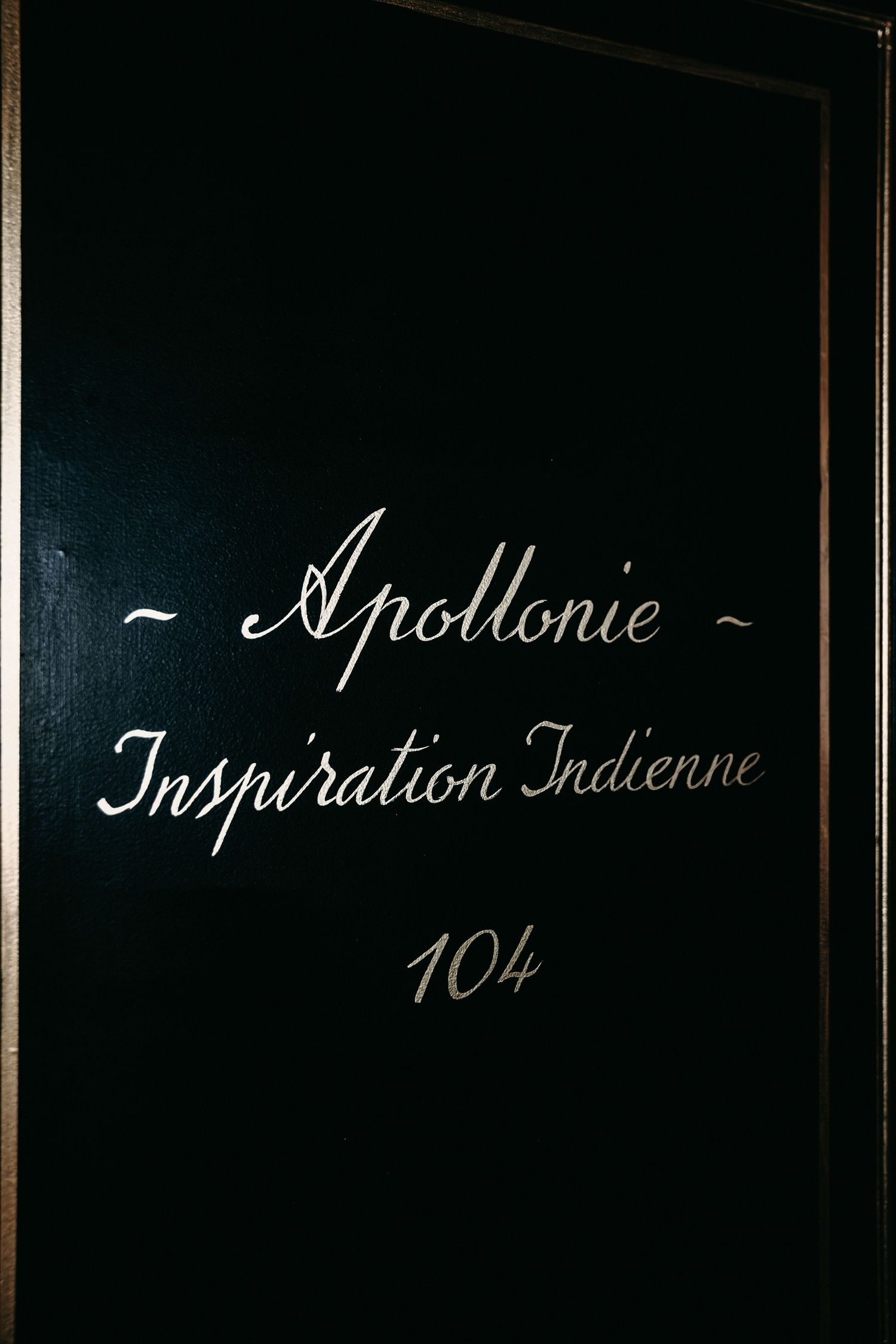 Elegant restaurant interior with dark walls and chalkboard menu displaying 'Apollonie' and 'Inspiration Indienne 104'.