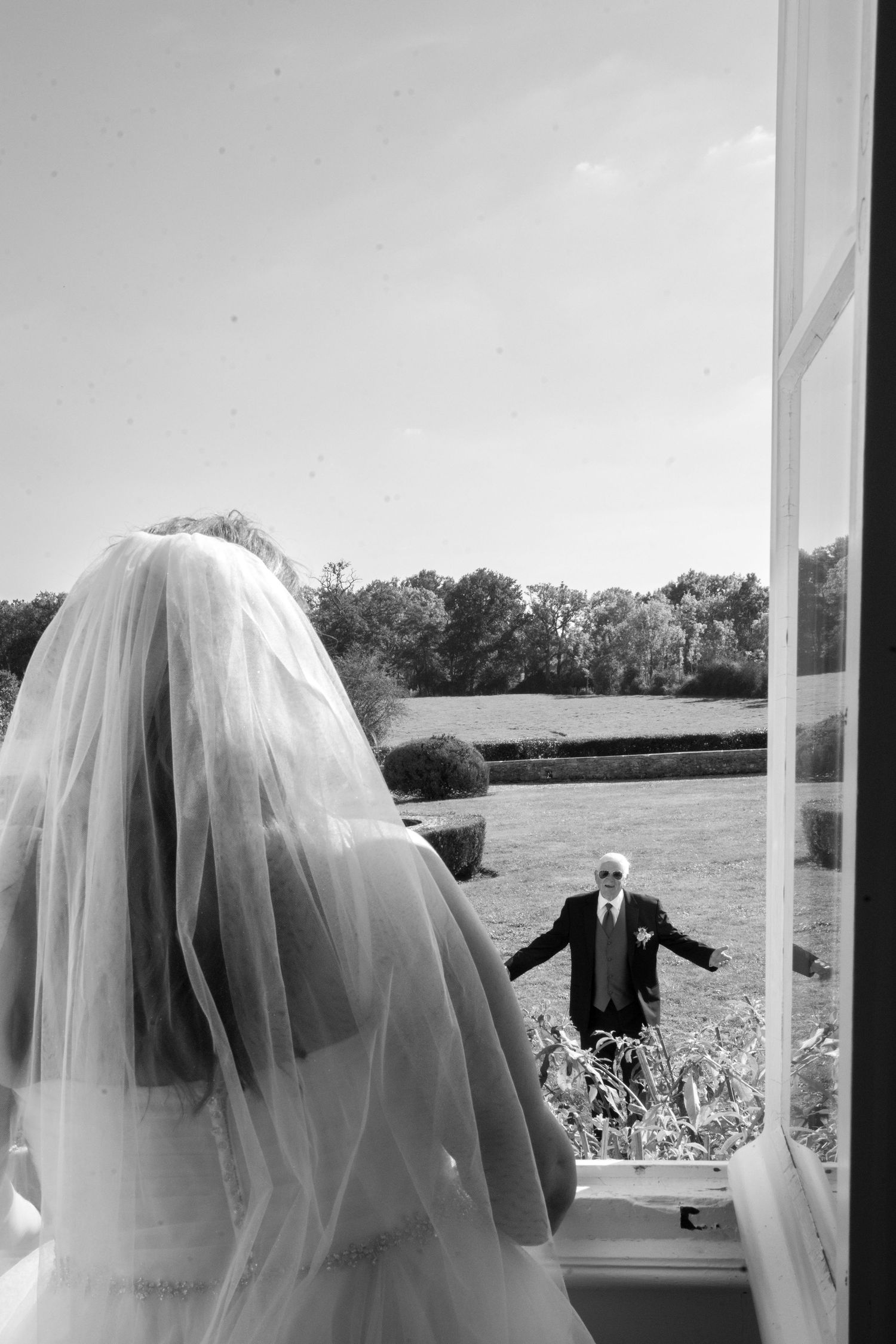 Bride in veil sees her father through window at château wedding near Paris, emotional black and white photography by Studio Reverie.