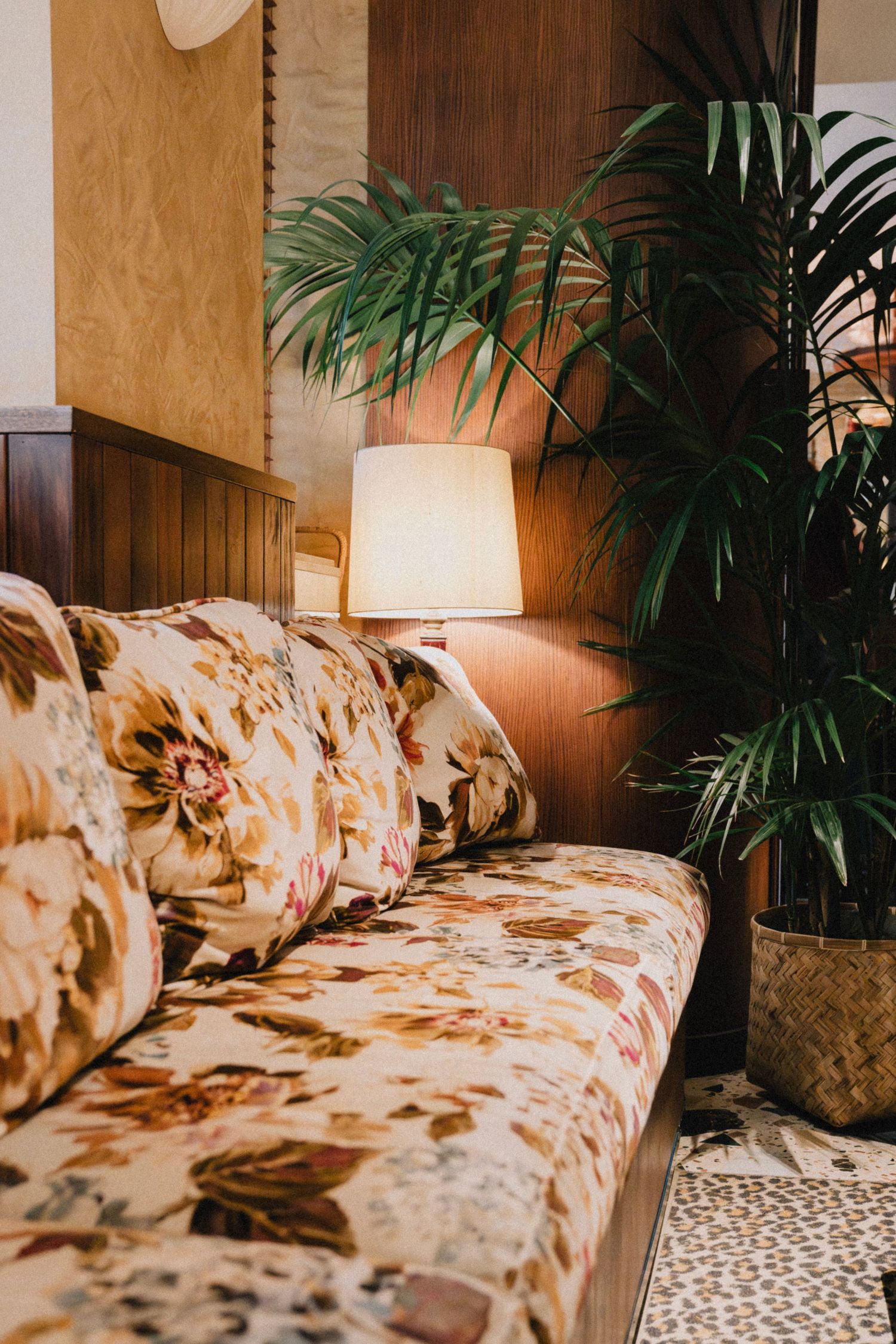 Vintage floral sofa with tropical plants and table lamps in an elegant lounge setting.